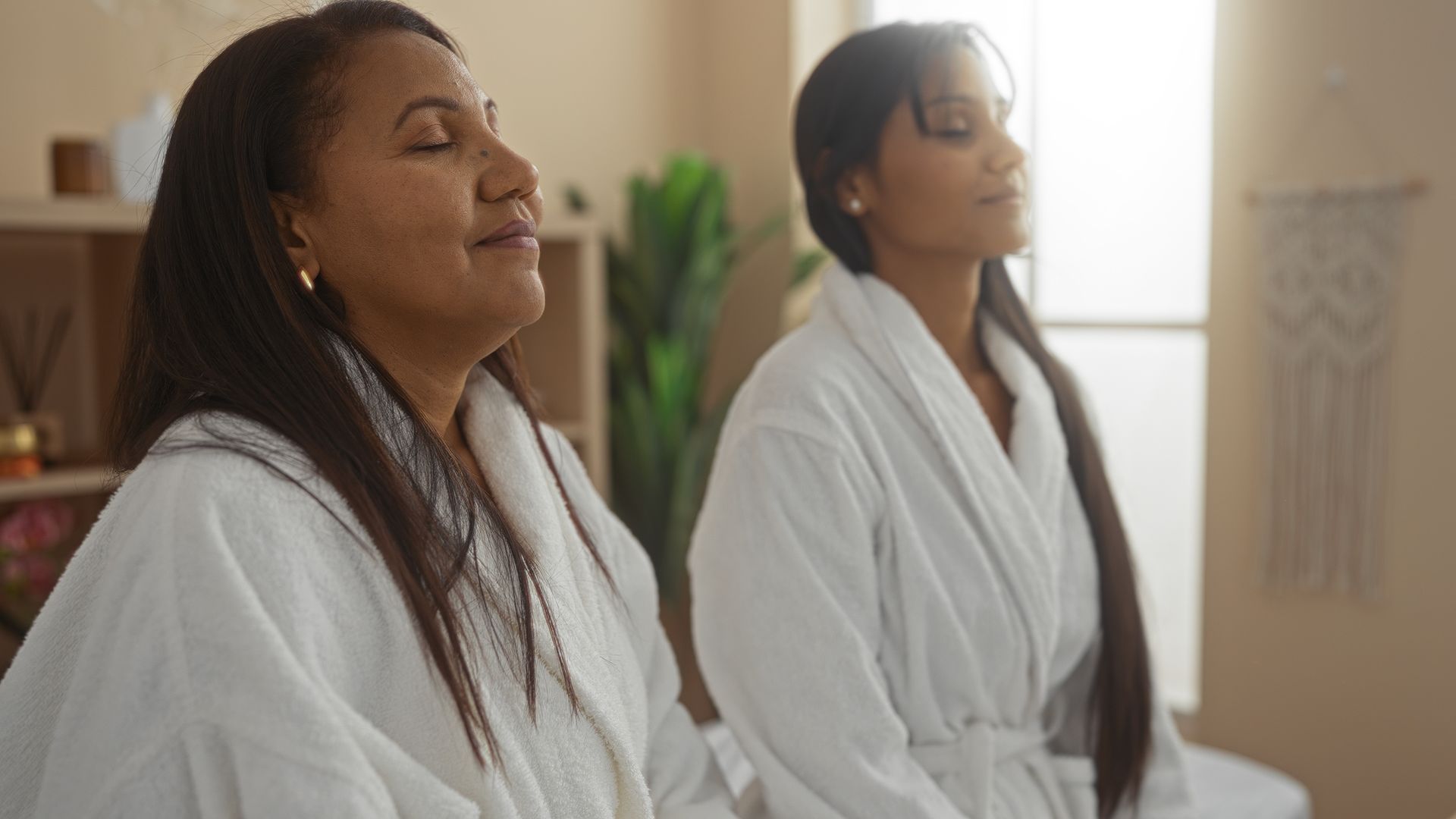 Two people in white spa robes sit with their eyes closed in a peaceful, relaxed setting.
