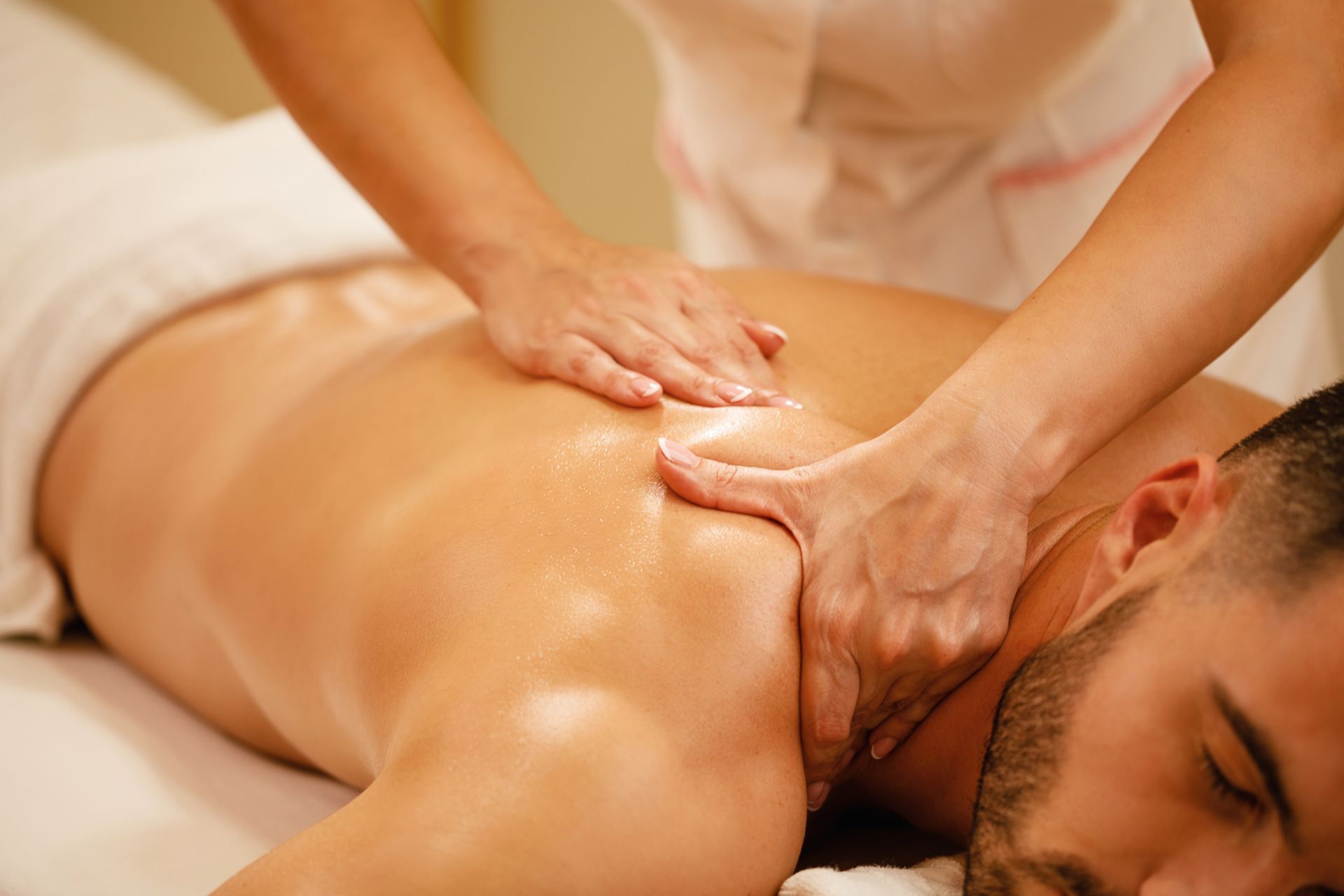 Person receiving a back massage in a spa. Hands massaging back and shoulder, white sheet, soft lighting.