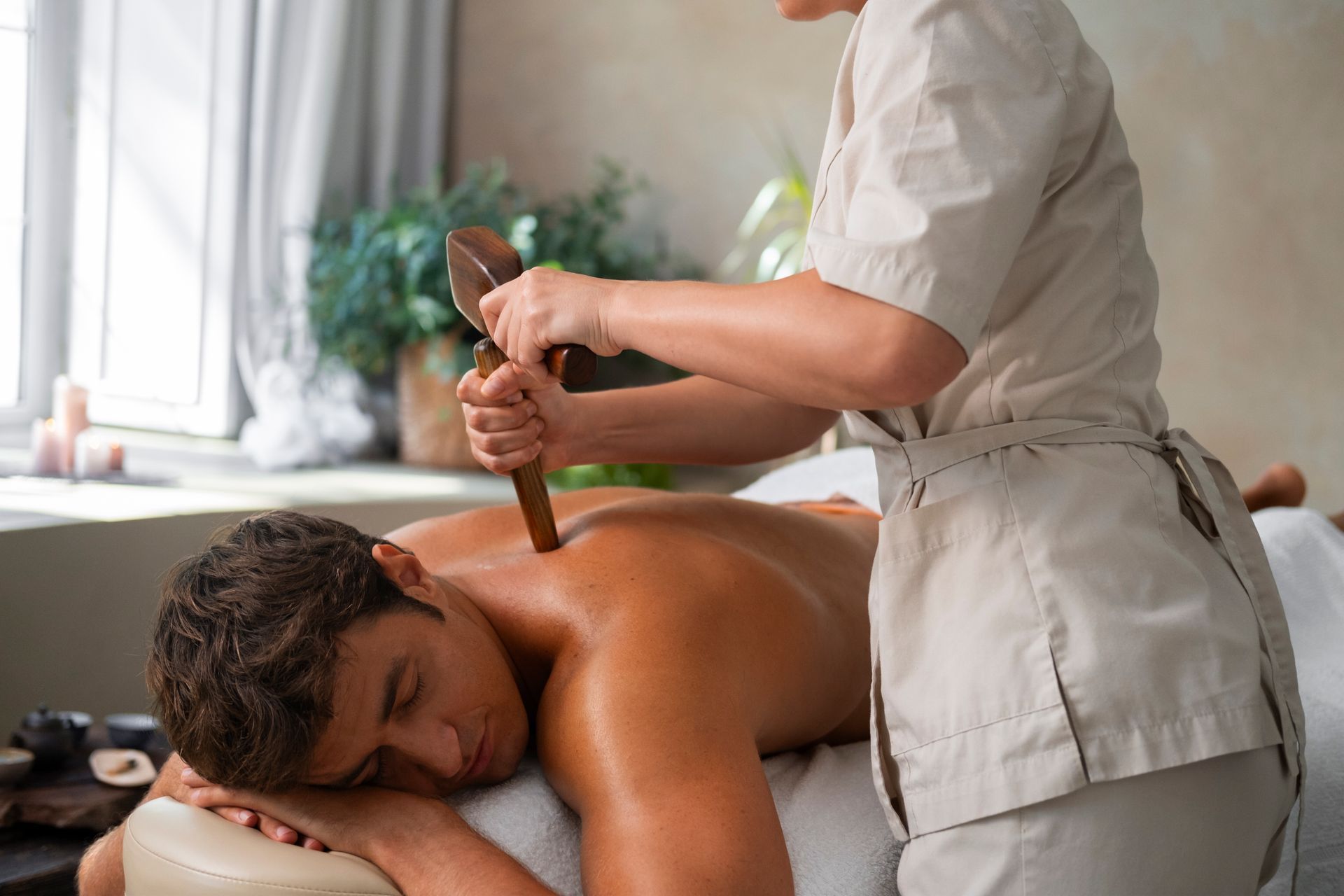 Man receiving a back massage with wooden tools at a spa.
