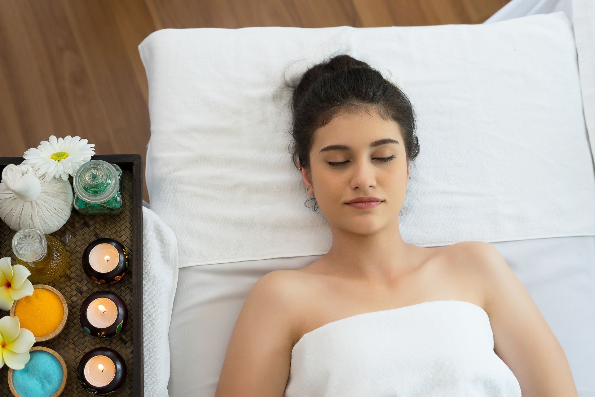 Woman relaxing on a massage table, spa setting. Candles, flowers, and spa treatments.
