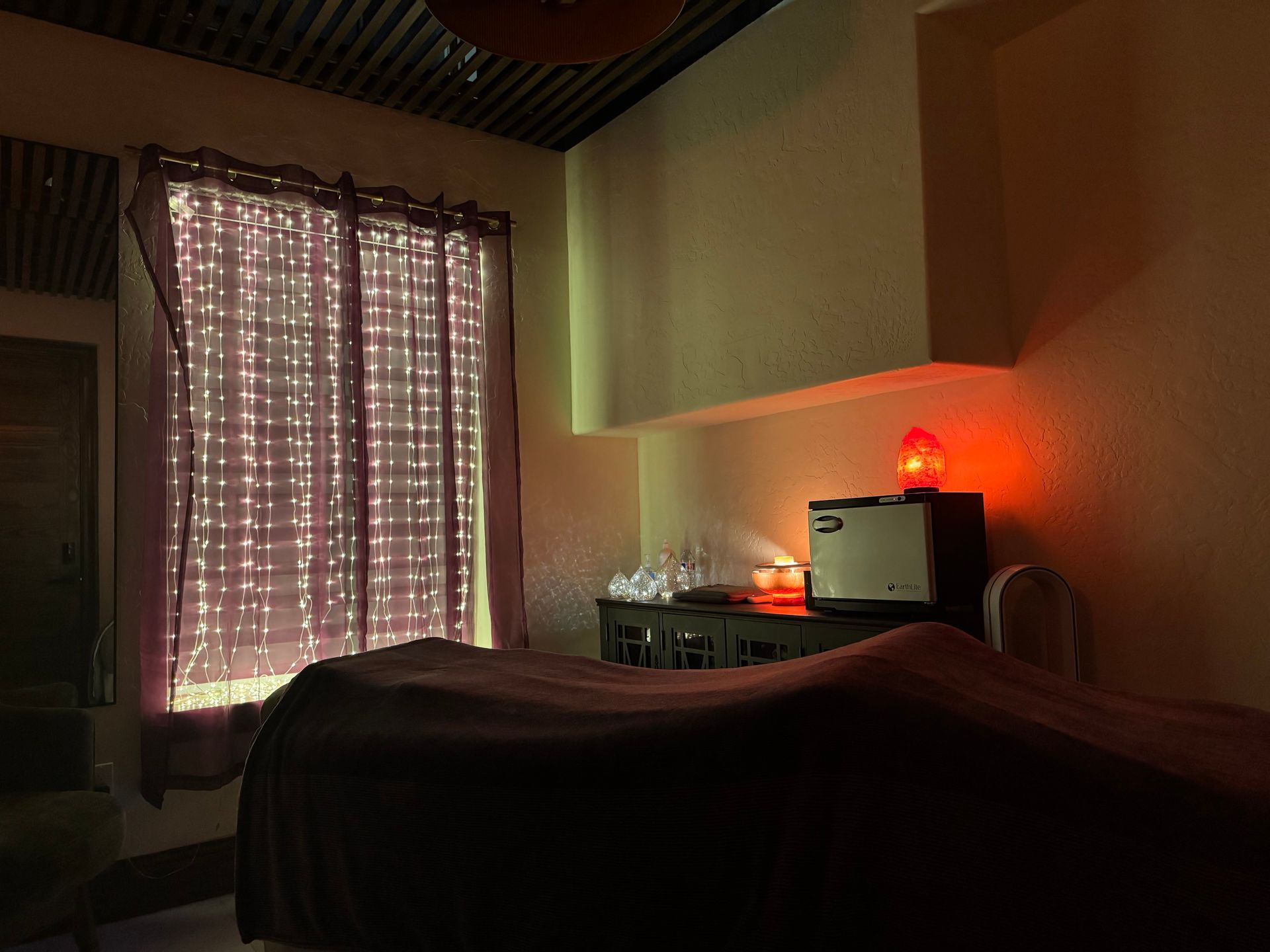 A room with a bed and a window with lights on it.