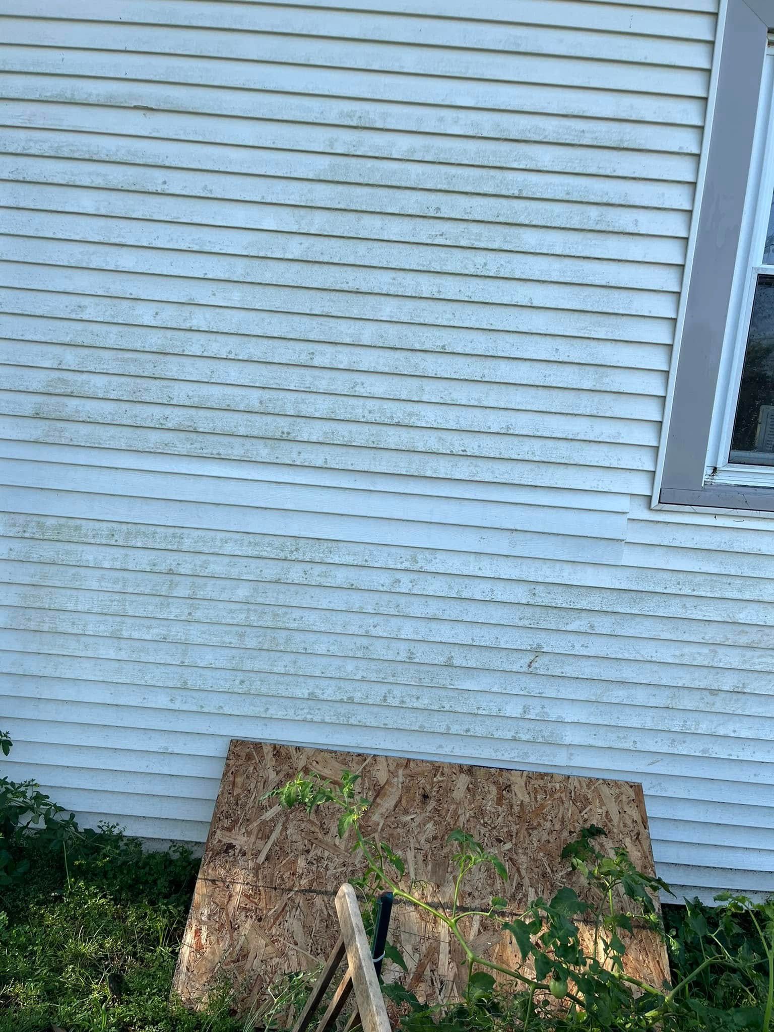 A white house with a window and a piece of plywood on the side of it.
