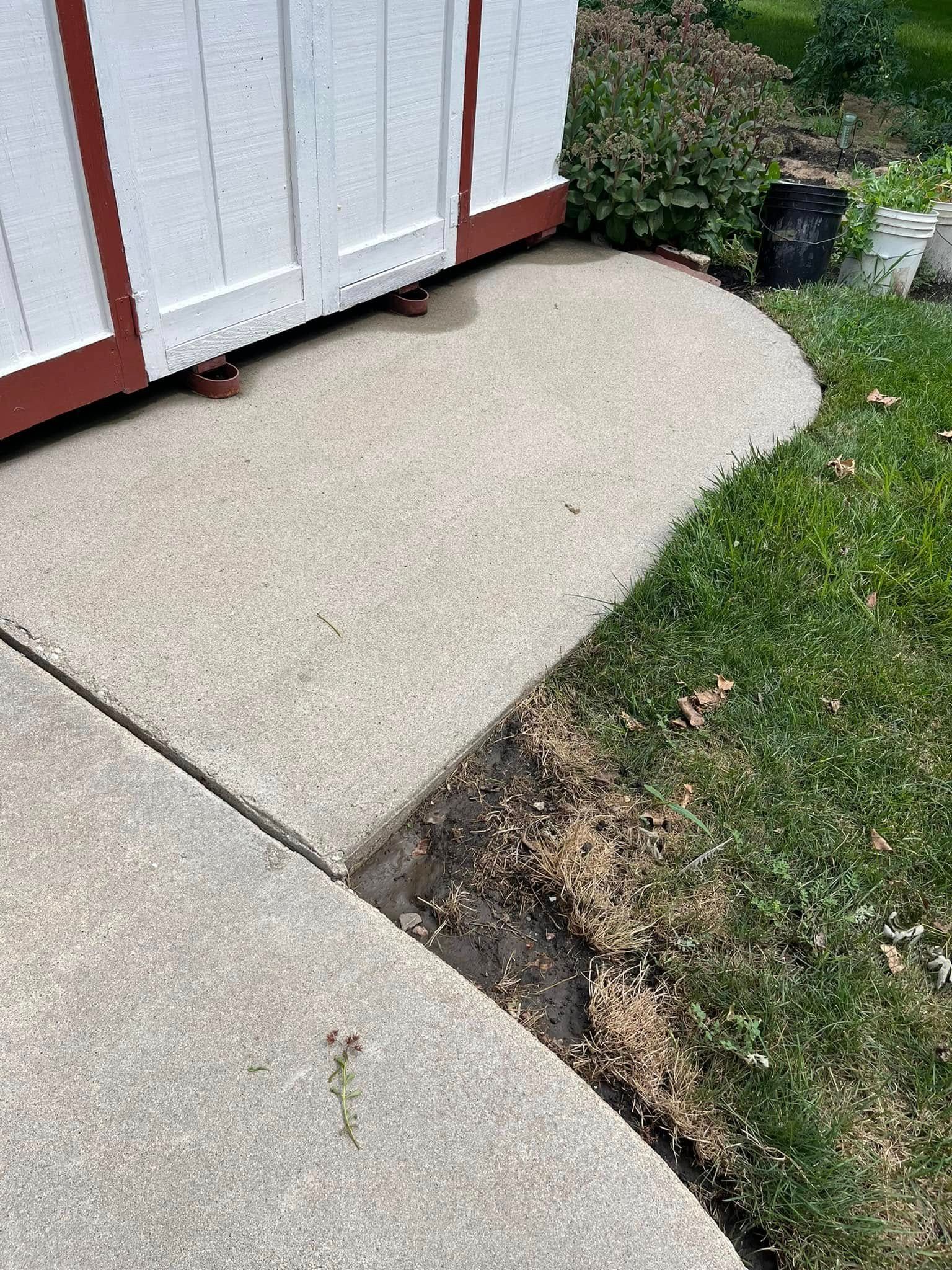 A concrete sidewalk next to a shed and grass.