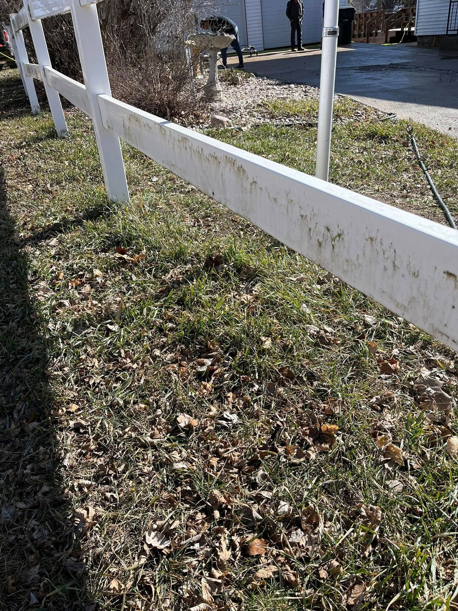 A white picket fence is surrounded by grass and leaves.