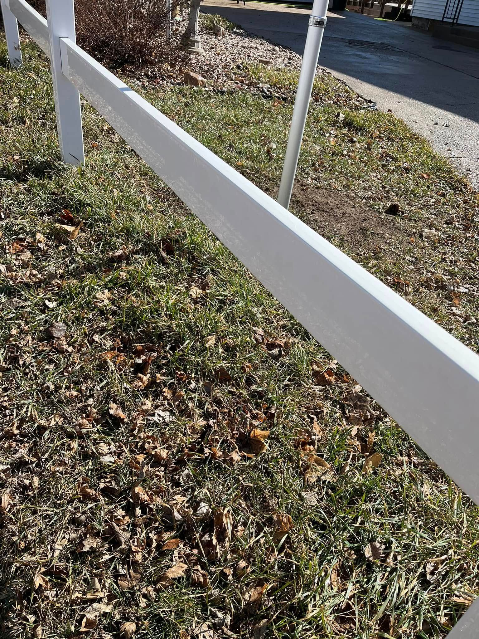 A white fence is surrounded by grass and leaves in a yard.