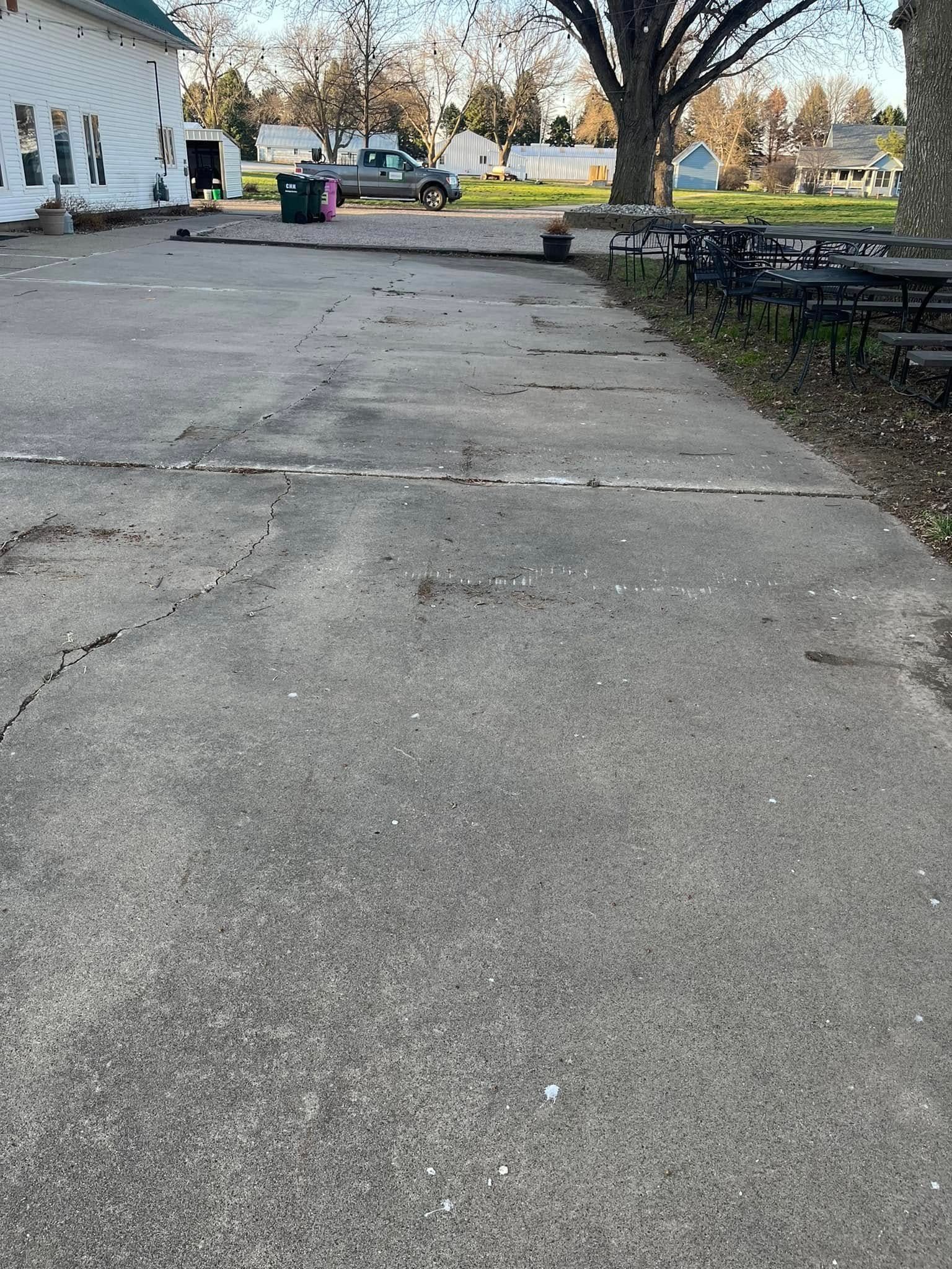 A parking lot with a white building in the background and a tree in the foreground.