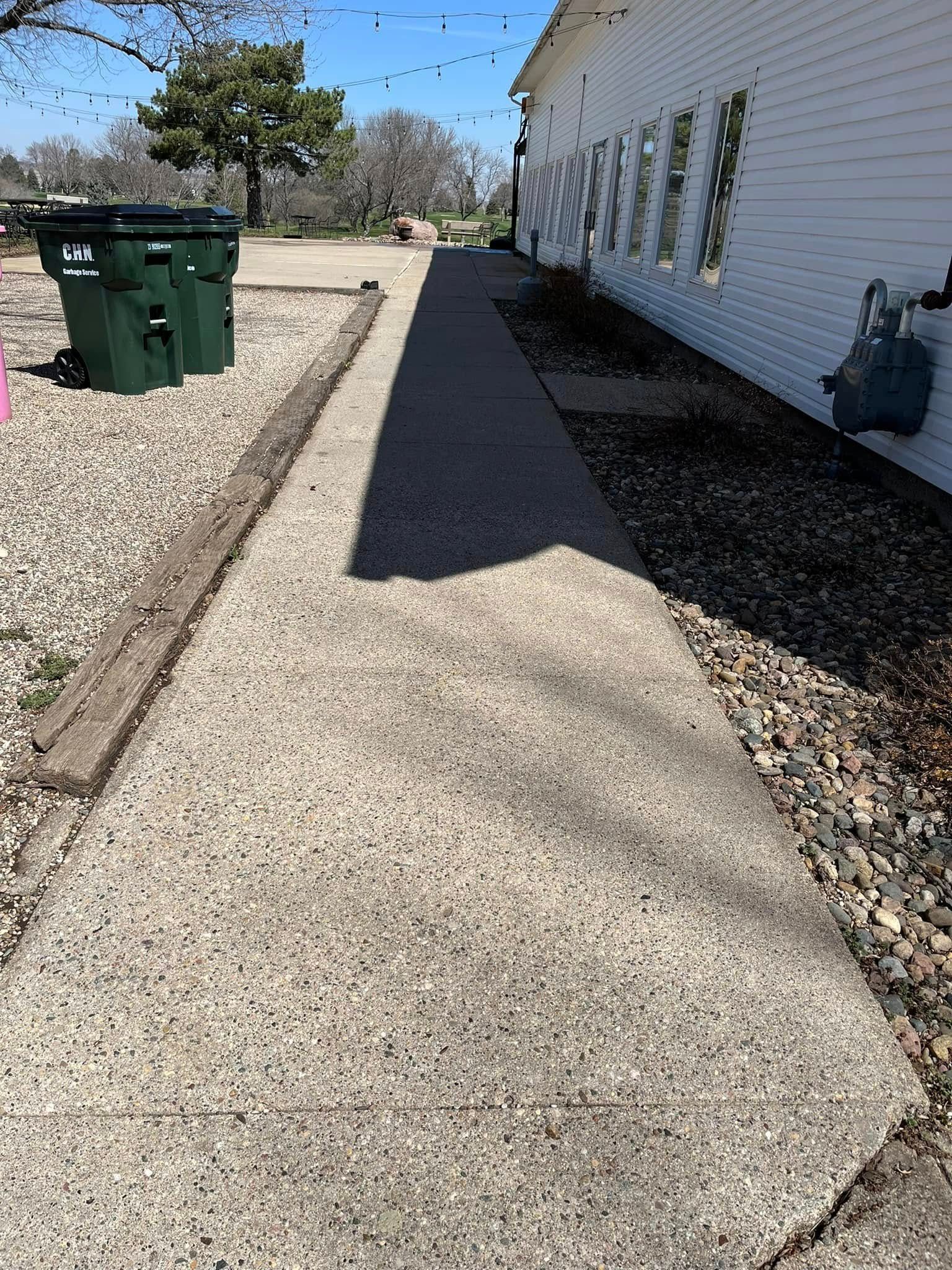 A sidewalk leading to a white building with green trash cans on the side.