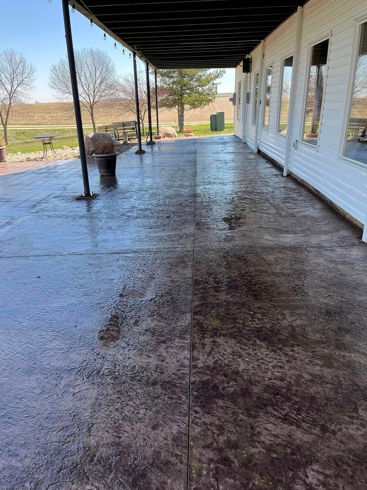 A covered porch with a concrete floor and a white building in the background.