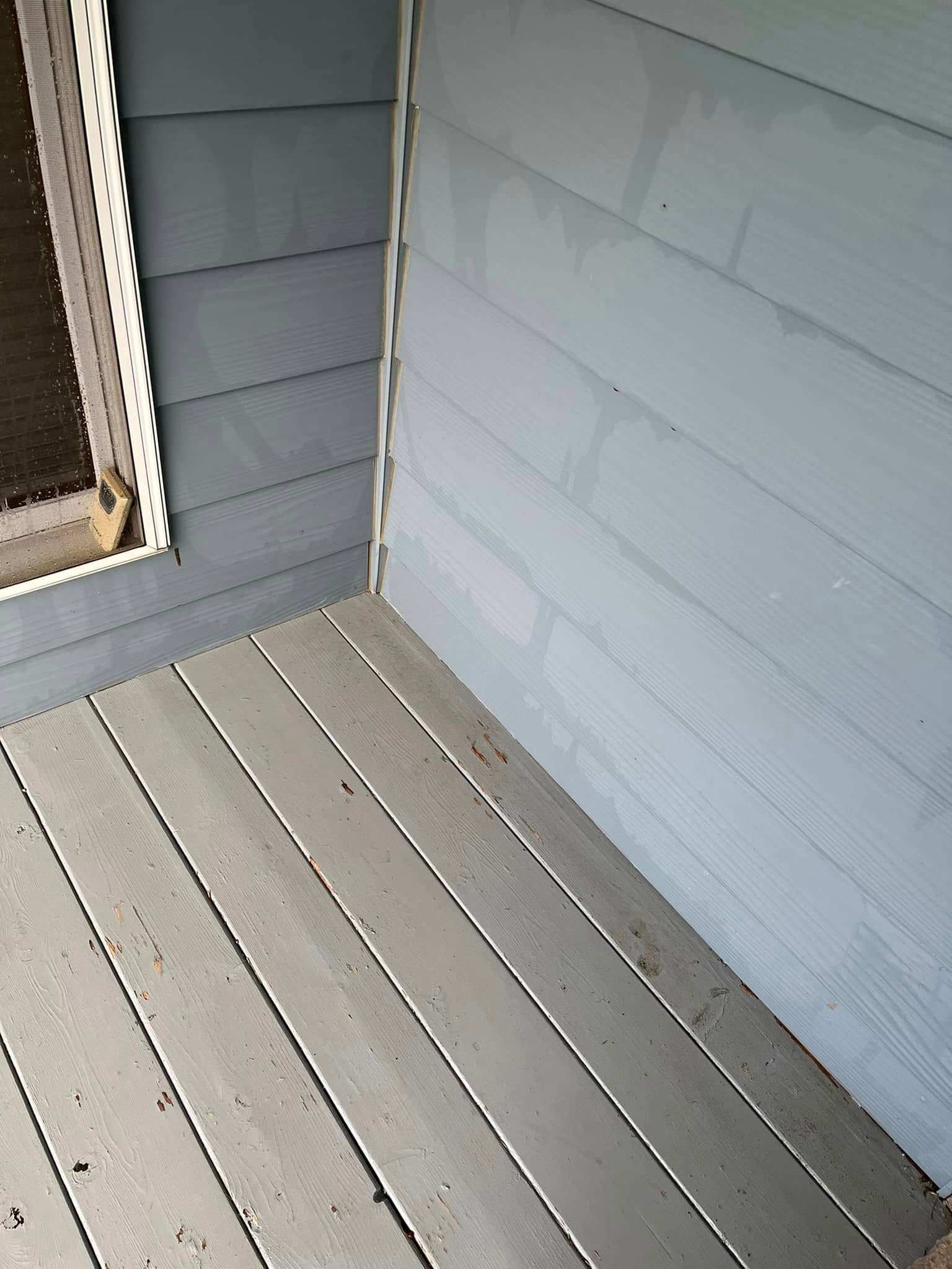 A corner of a house with a window and a wooden deck.