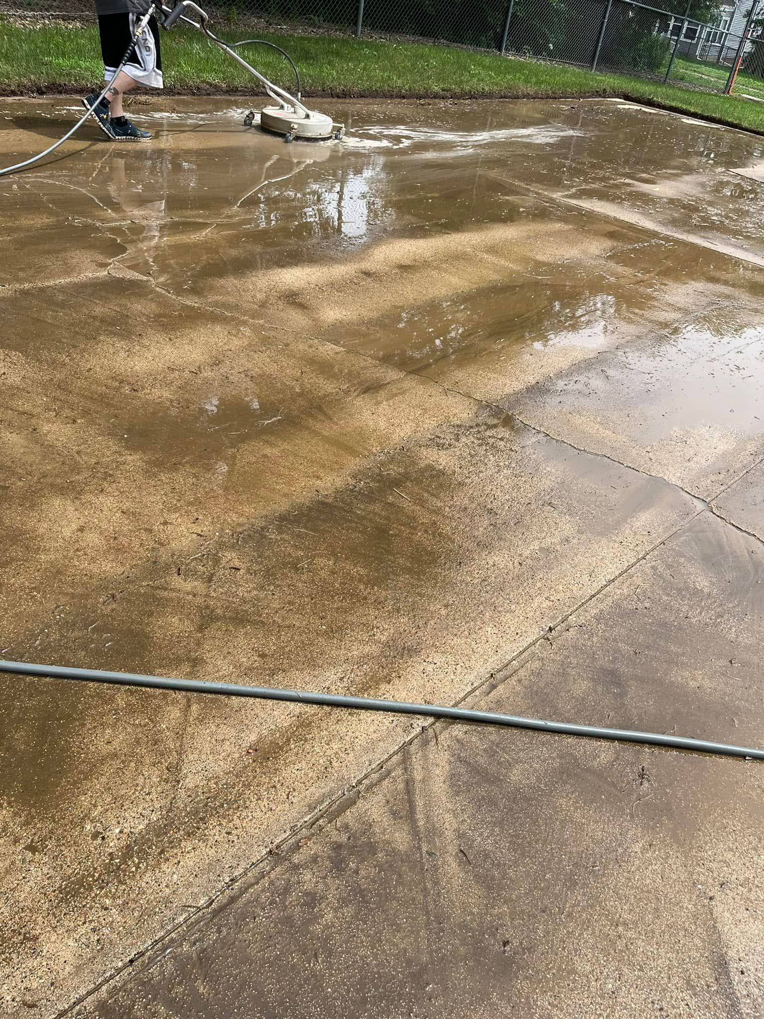A person is cleaning a concrete driveway with a mop.