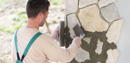 A man applying mortar between stone tiles on a wall.