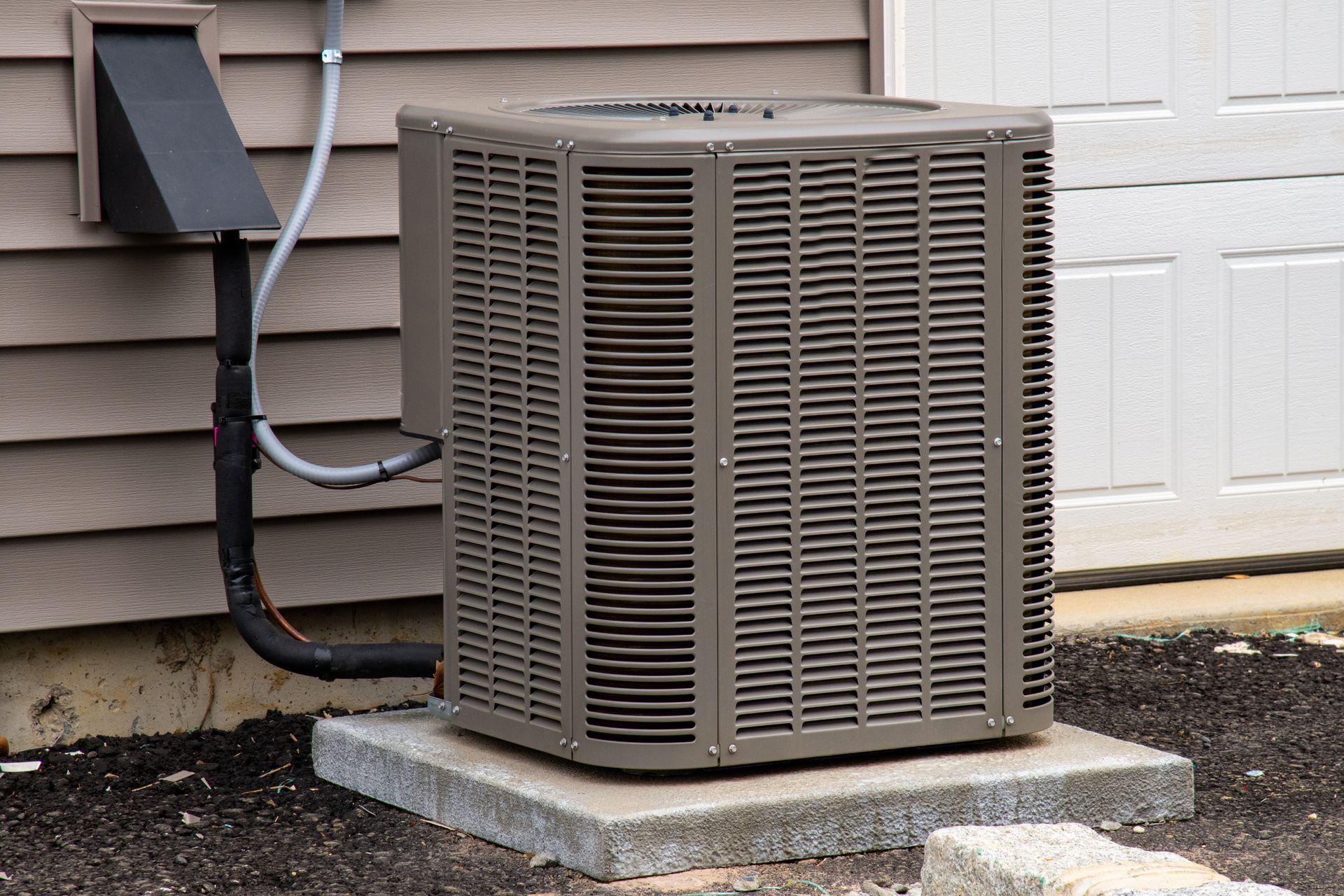 Gray air conditioning unit on a concrete pad next to a house wall and a white door.