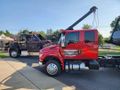 A red tow truck is parked next to a black tow truck on the side of the road.