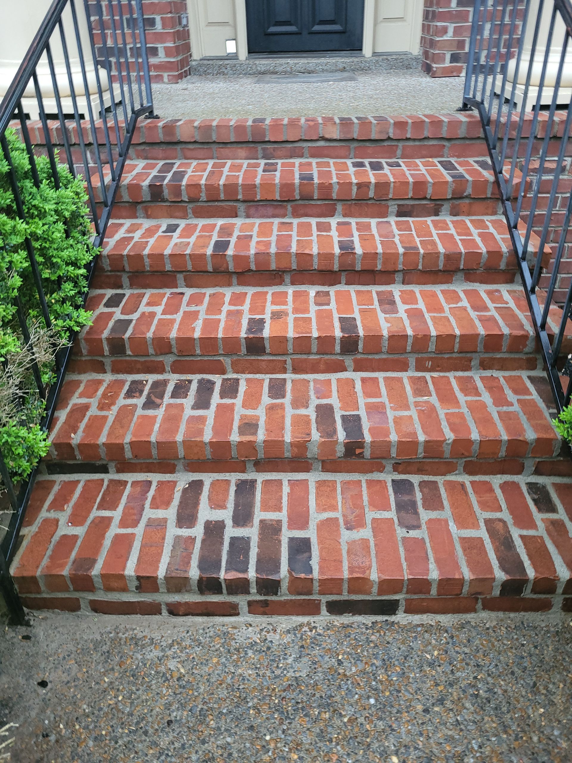 A set of brick stairs leading up to a house with a wrought iron railing.