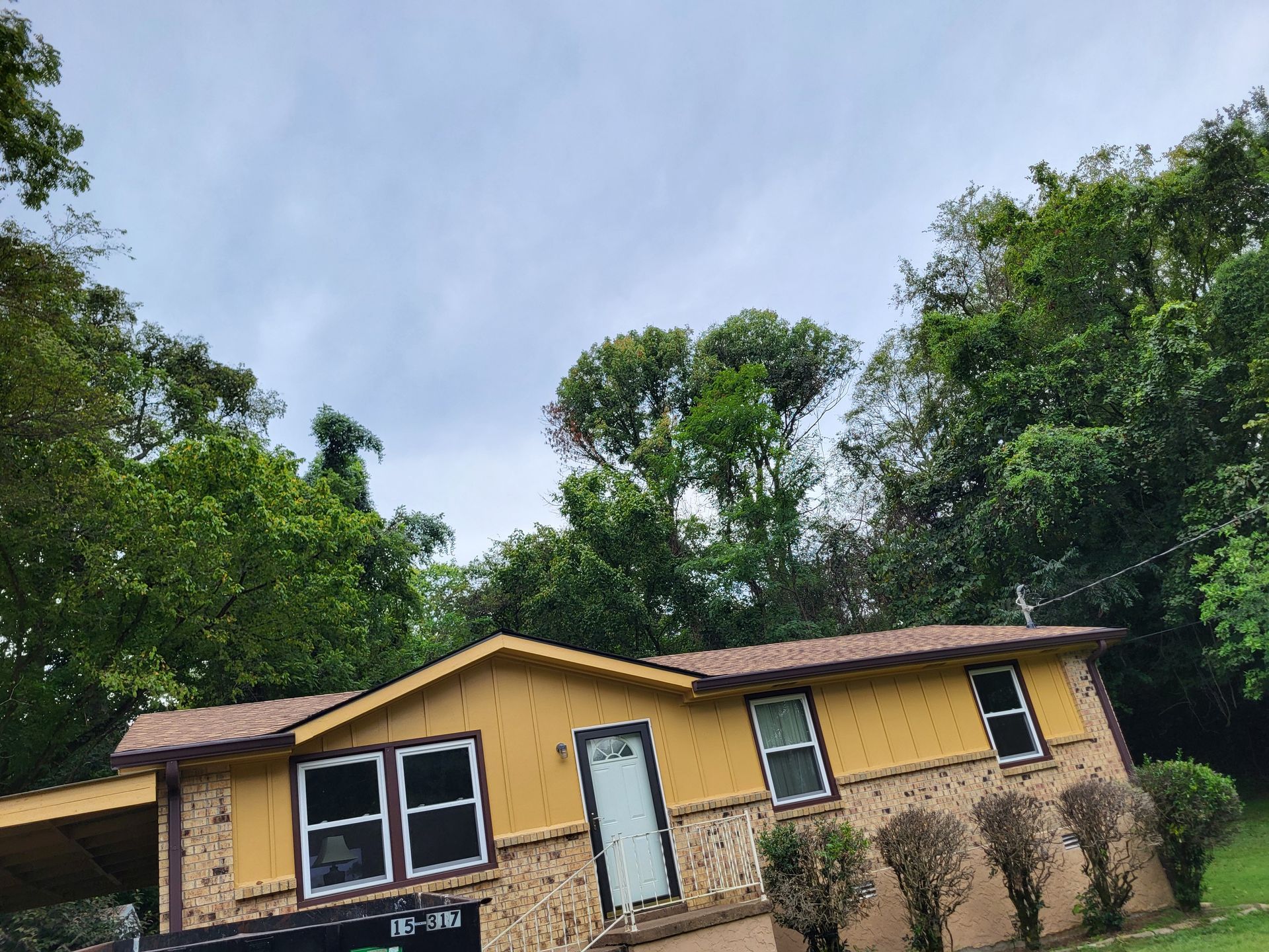 A yellow house with a brown roof is surrounded by trees.