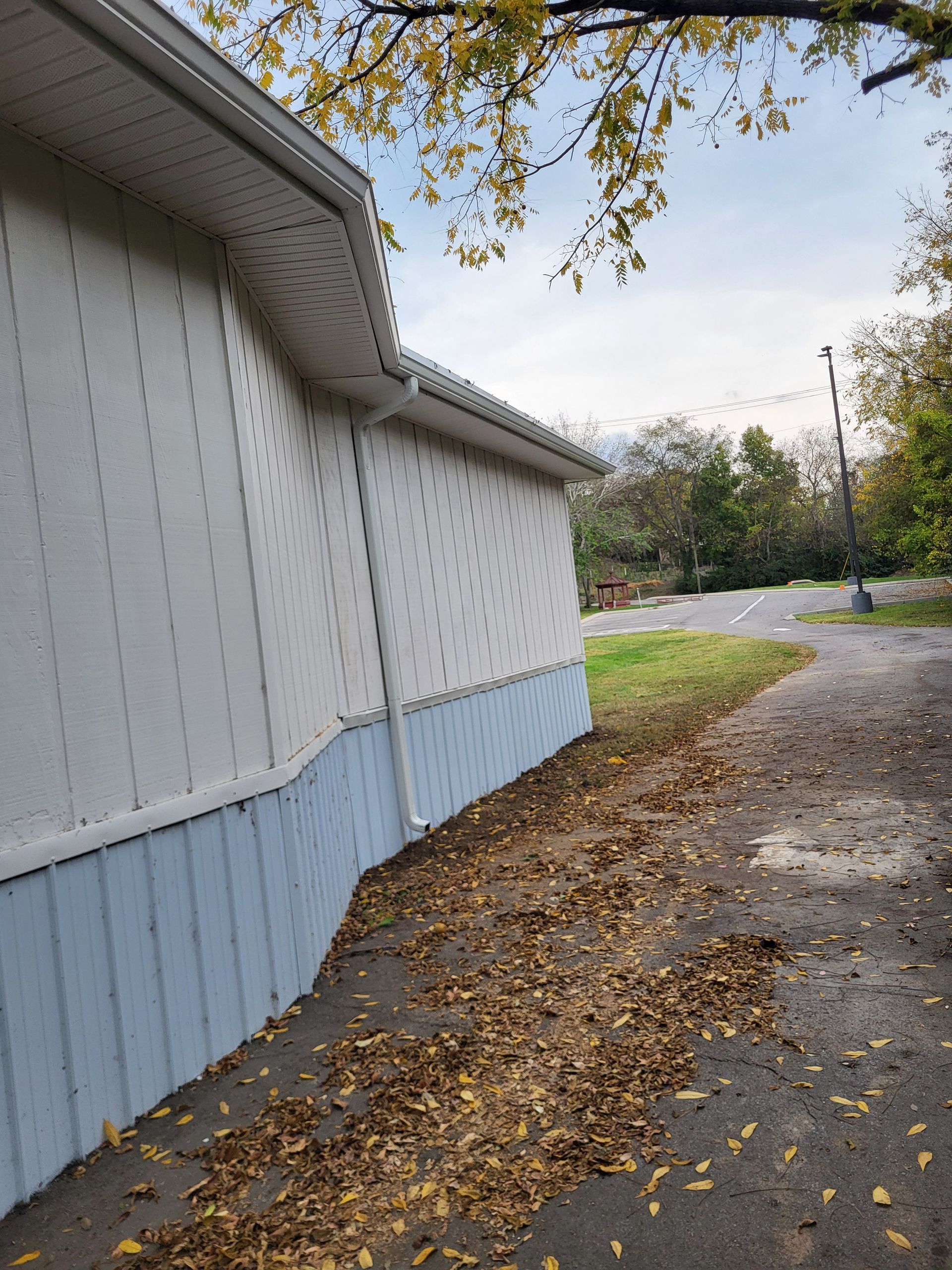 A sidewalk leading to a house with leaves on the ground.