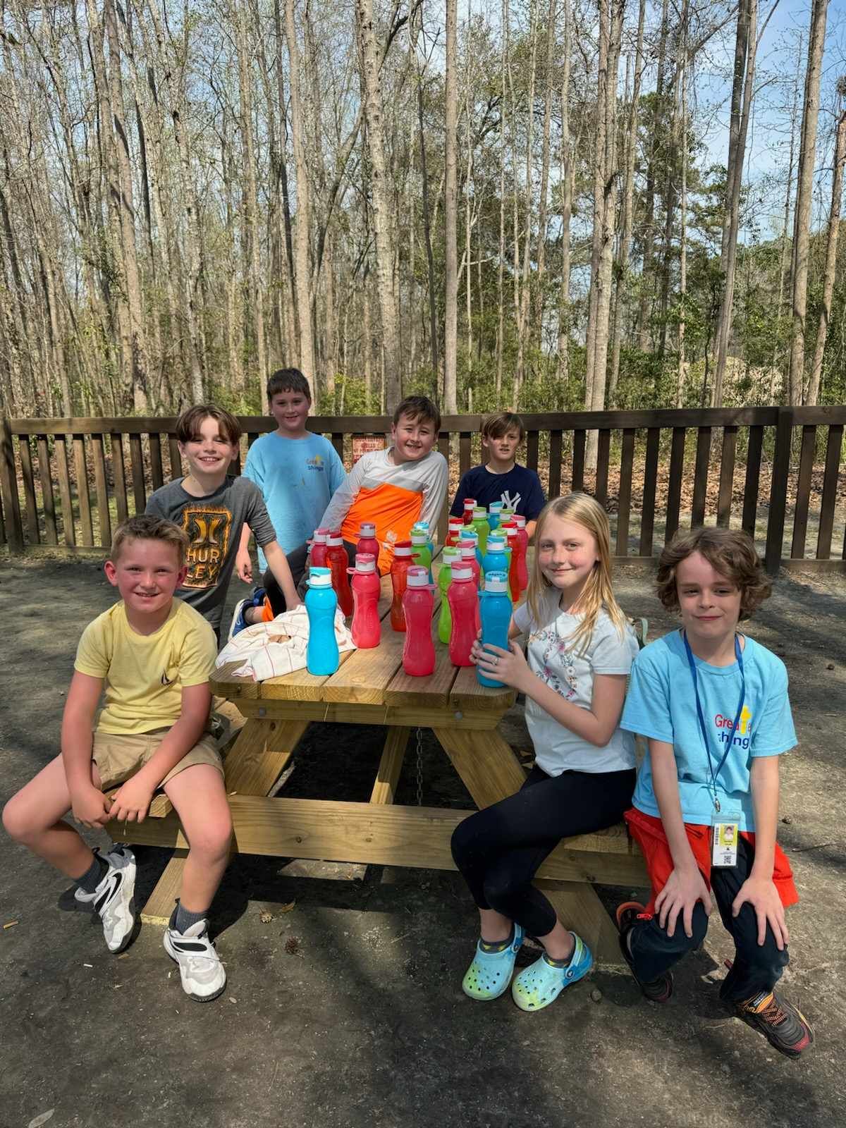 A group of children are sitting at a picnic table with water bottles.