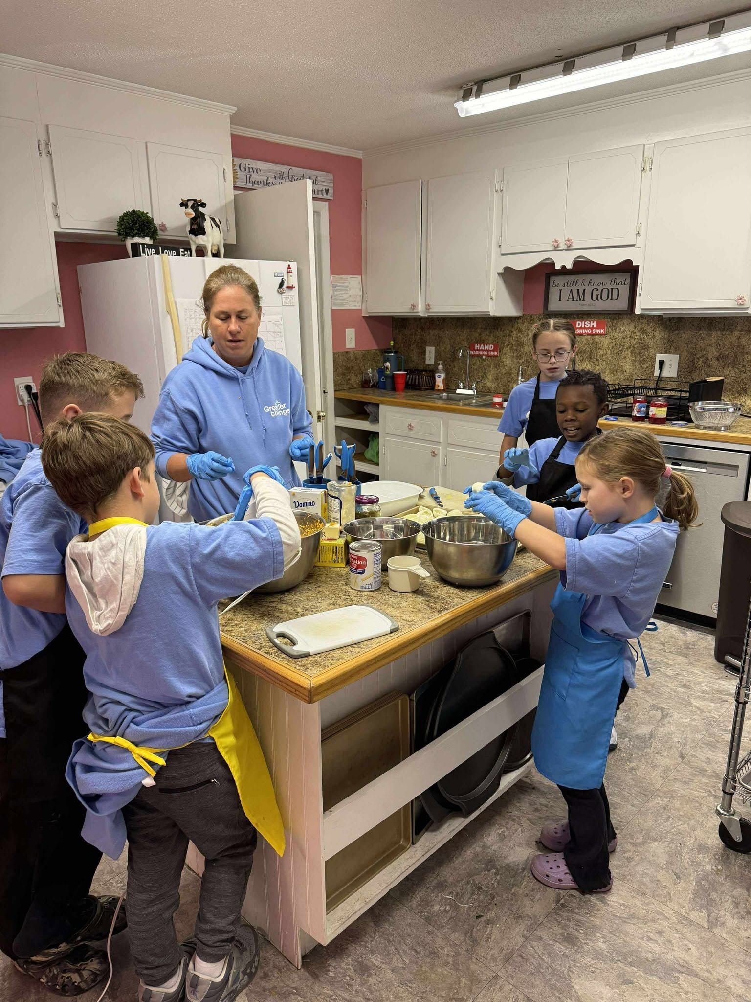 A group of children are standing around a kitchen counter preparing food.