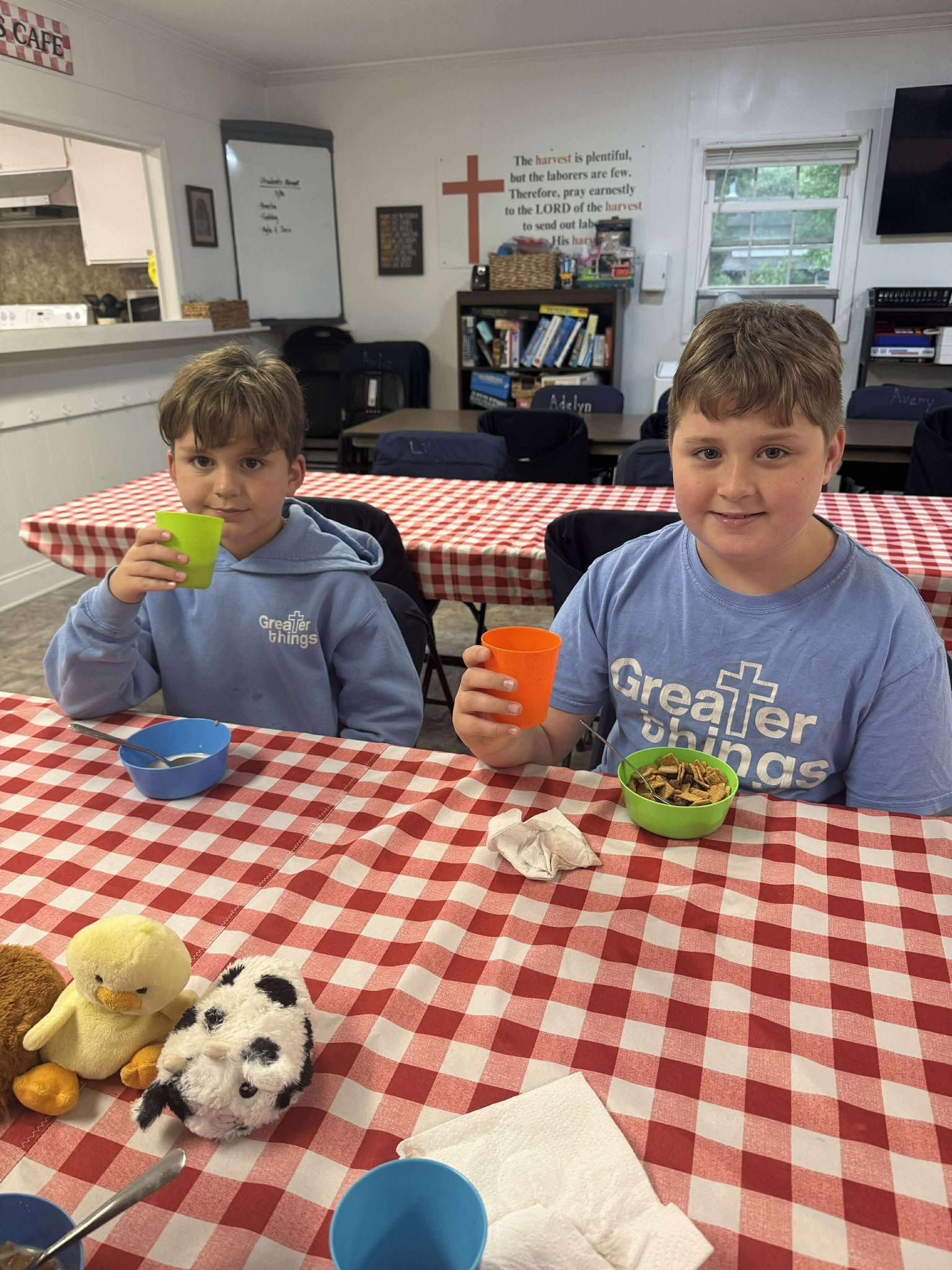 Two young boys are sitting at a table drinking from cups.