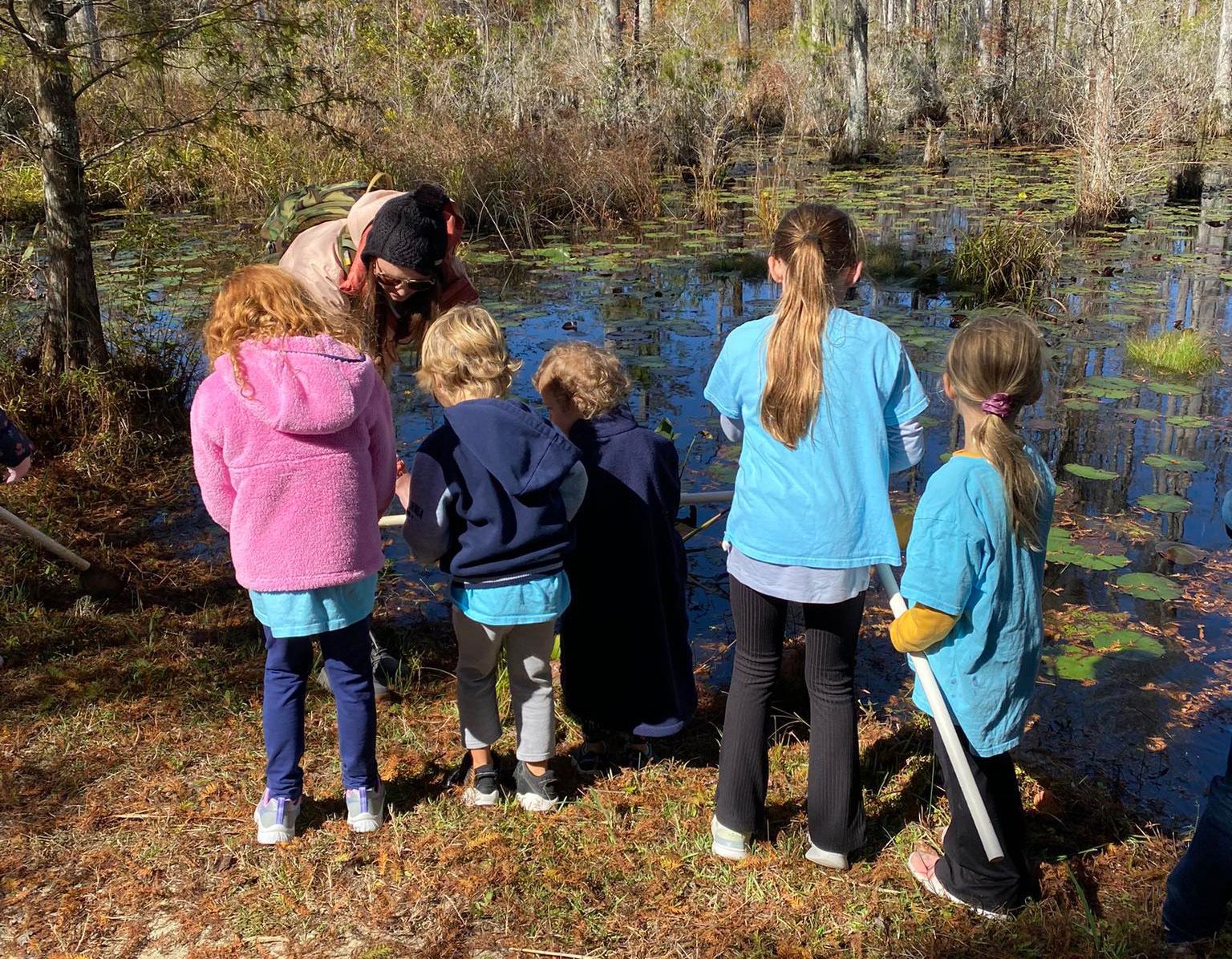 A group of children are looking at a pond.