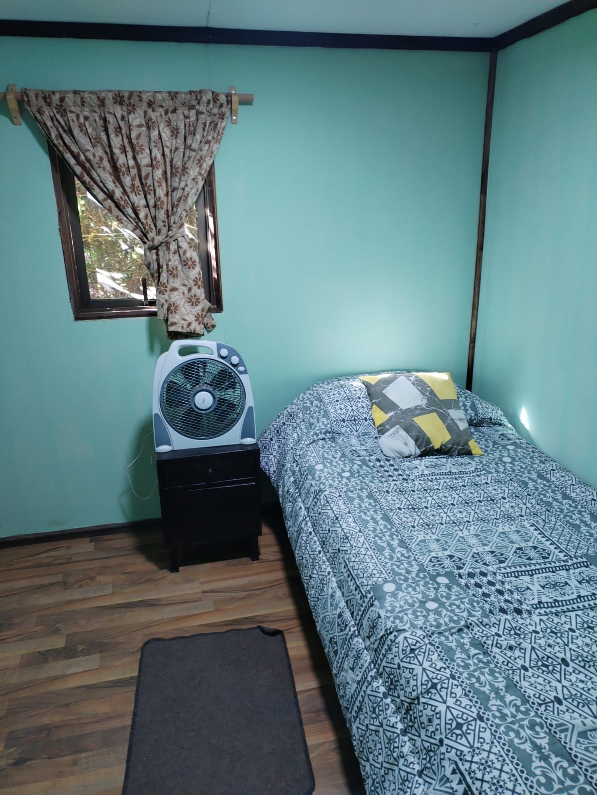 Un dormitorio con cama, mesita de noche, ventilador y ventana.