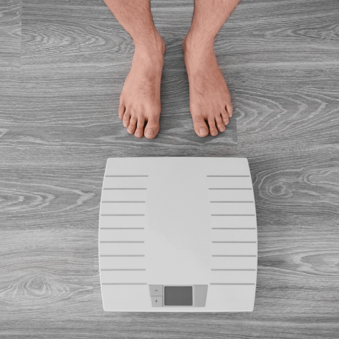 A man is standing on a scale on a wooden floor.