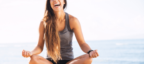 A woman is sitting in a lotus position on the beach.