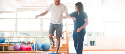 A woman is helping a man do exercises in a gym.