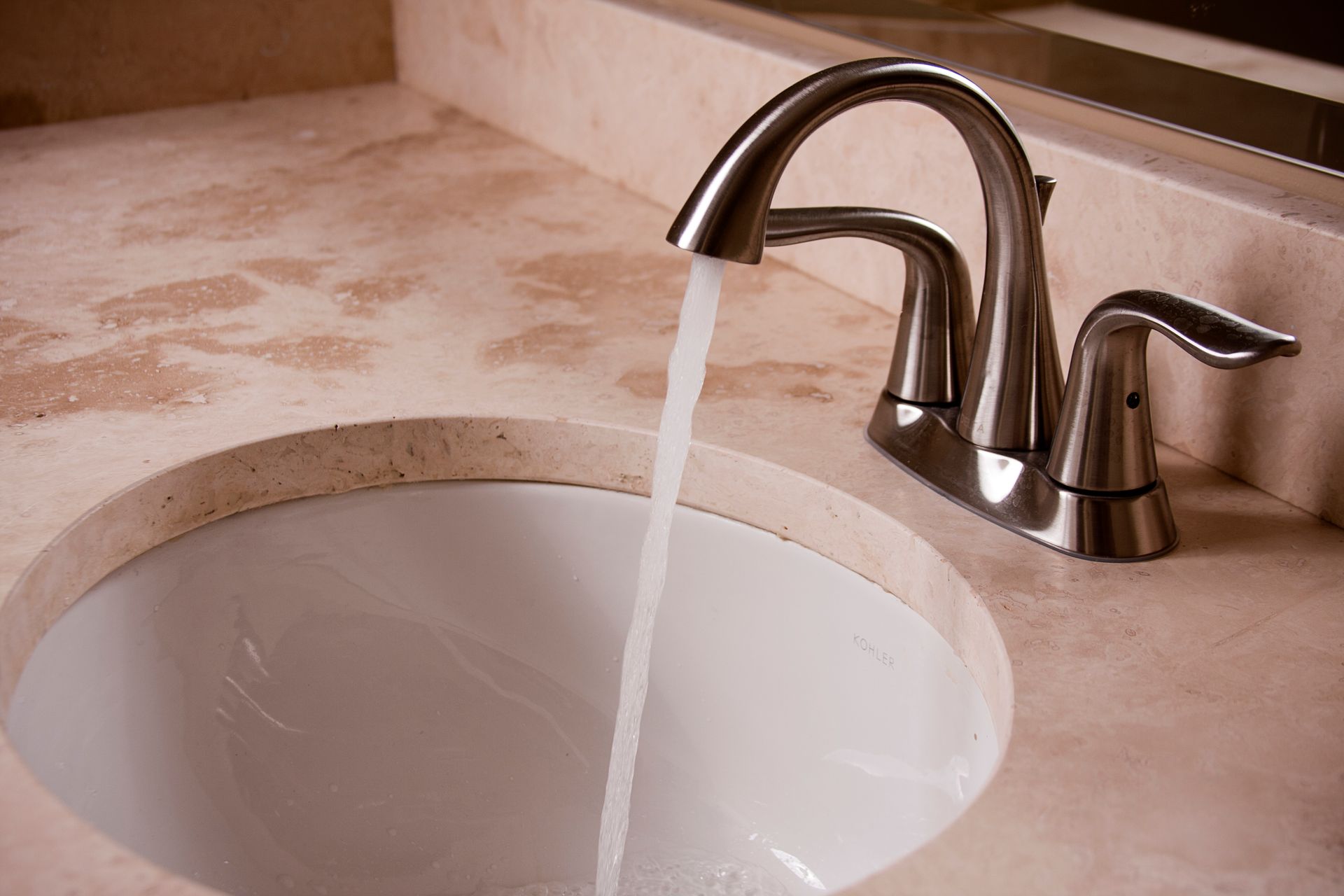 Bathroom sink with chrome faucet running water into a white basin on a beige countertop