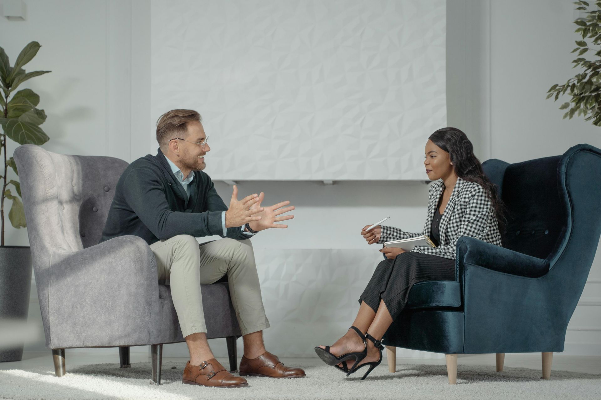 A professional conversation between two people sitting in upholstered armchairs in a bright, modern office space.