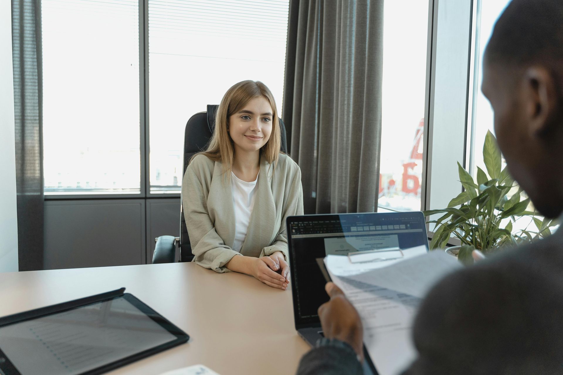 A professional interview is taking place in an office, with a candidate smiling at a recruiter reviewing their documents.