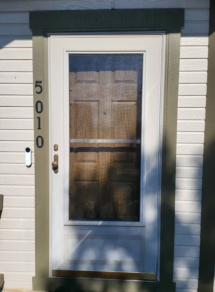 Front door with screen. House number 5010. White door with dark screen, surrounded by green trim.