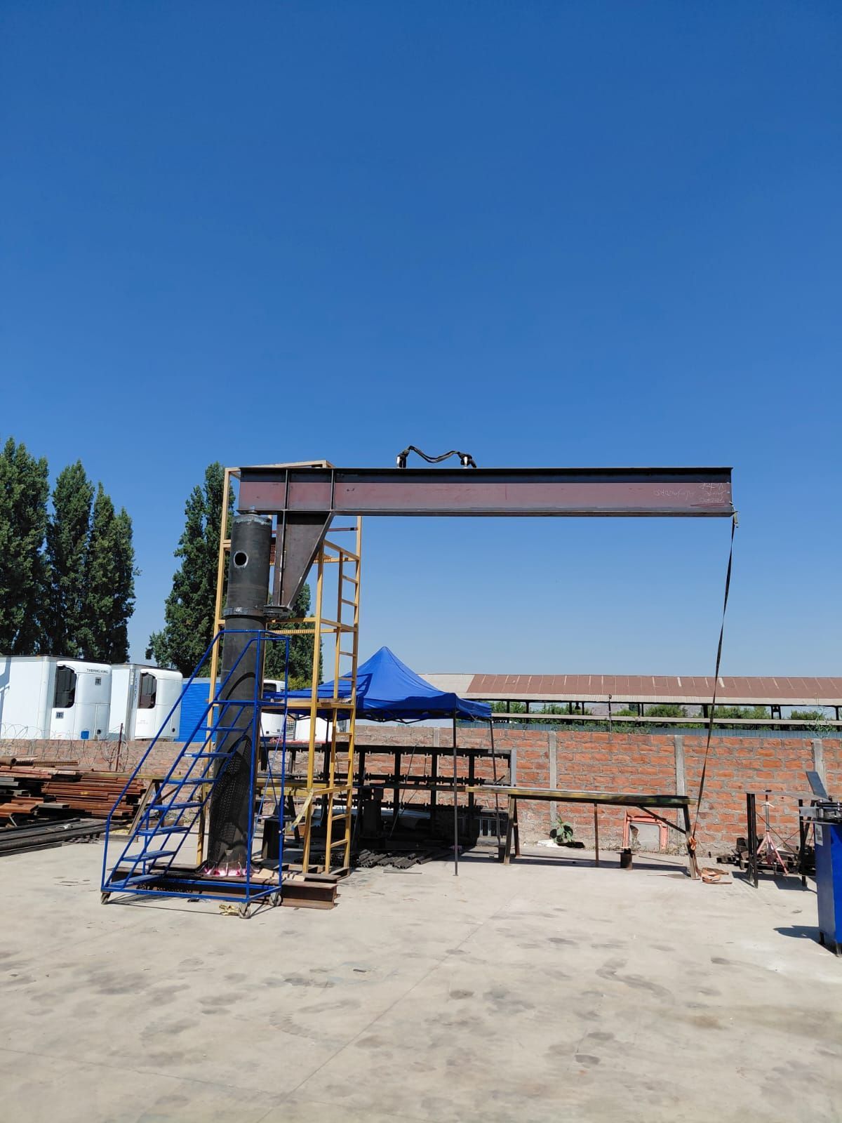 Una grúa pórtico con una viga marrón contra un cielo azul. Tiene una escalera y una plataforma acopladas.