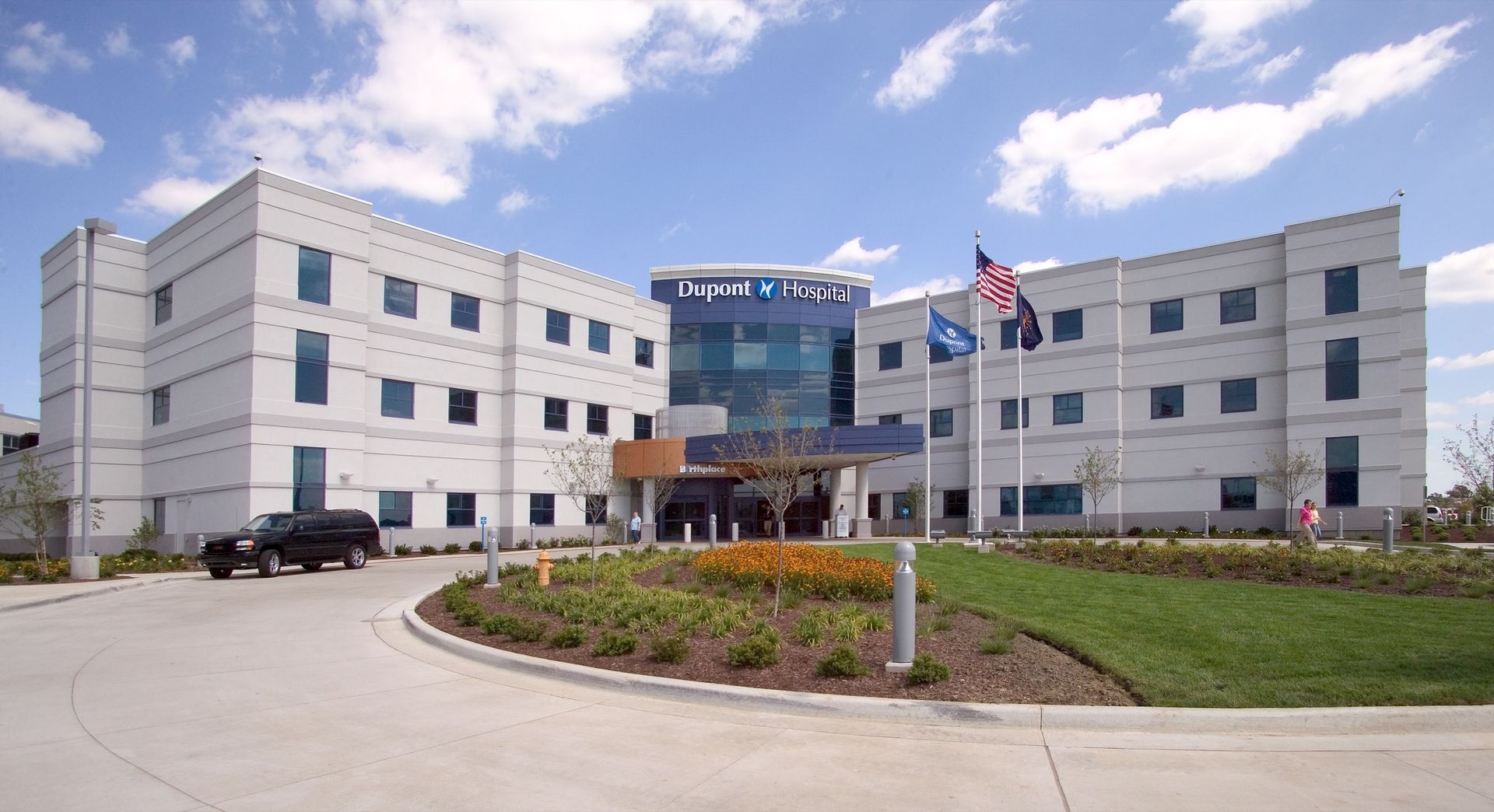 Modern hospital building with a curved driveway, flags, and landscaped entrance of Dupont Hospital in Fort Wayne