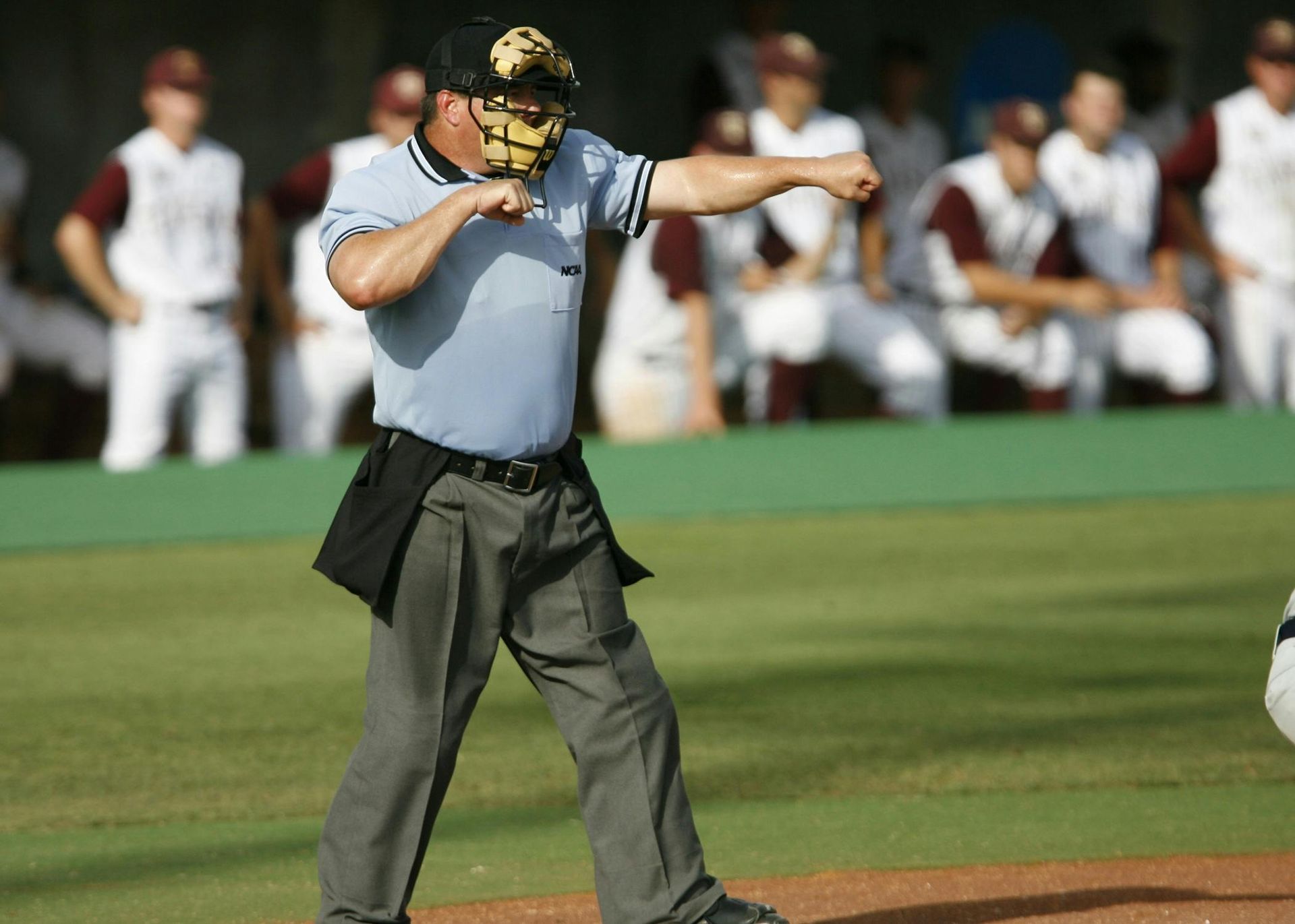 Baseball umpire signaling a call on the field-Out, with players blurred in the background.