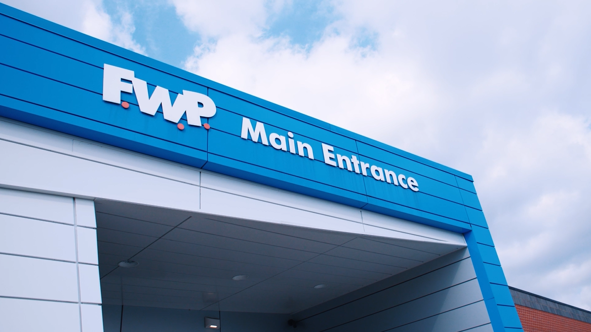 FWP Main Entrance sign above a blue-framed building entrance under a partly cloudy sky