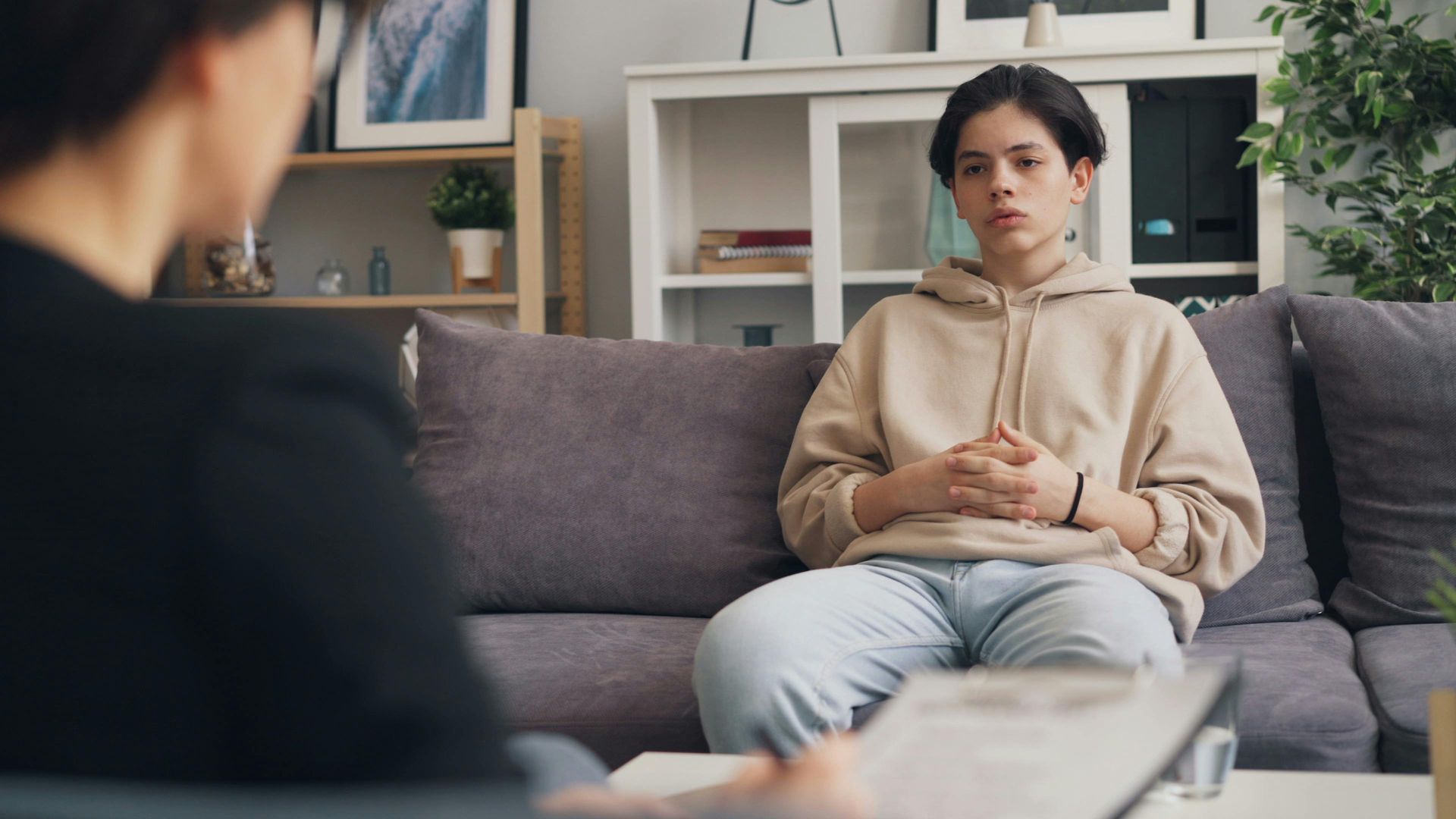 a teenage boy sitting on a couch talking to an adult