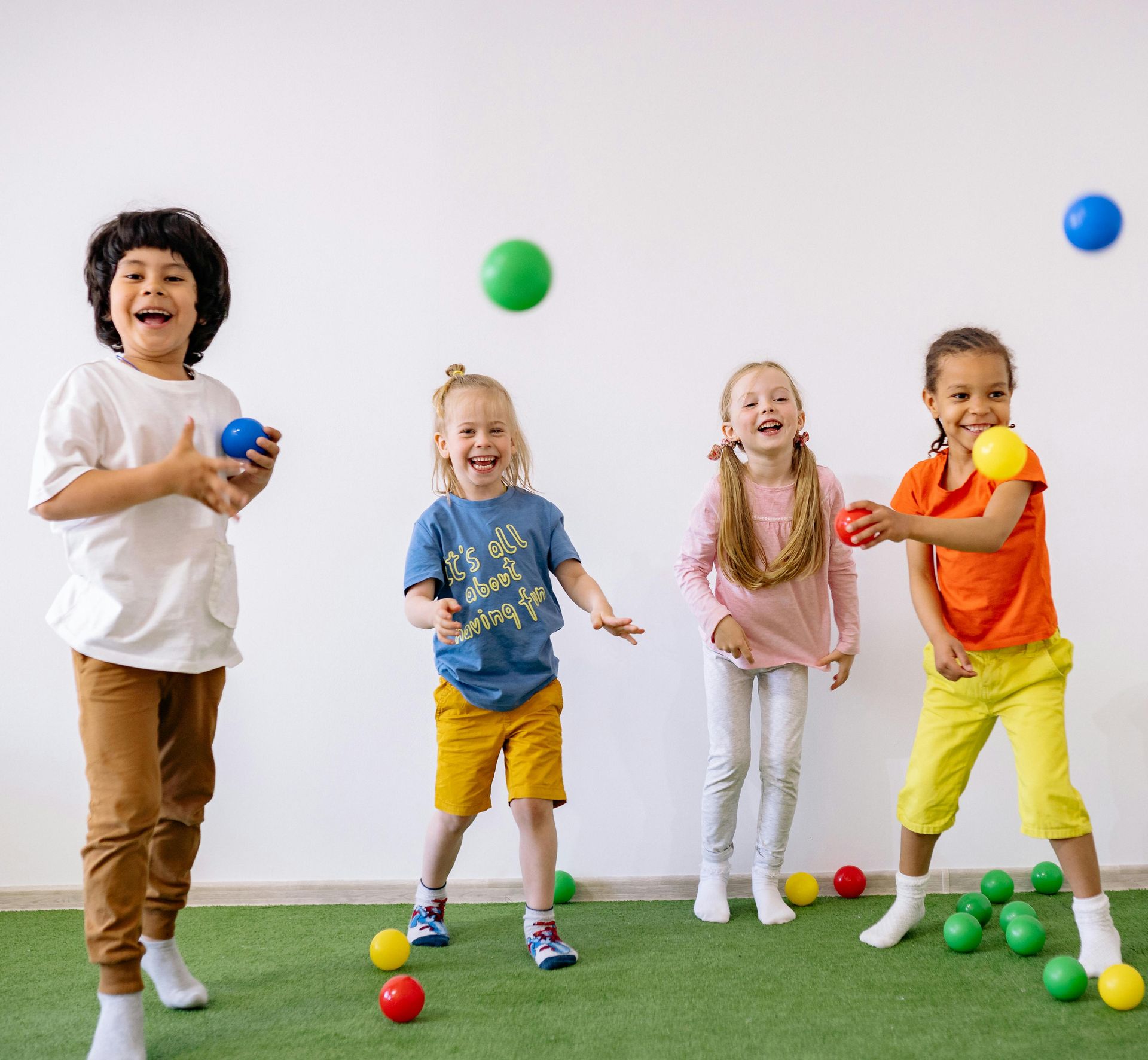 Children playing with colorful balls on green grass against a white background