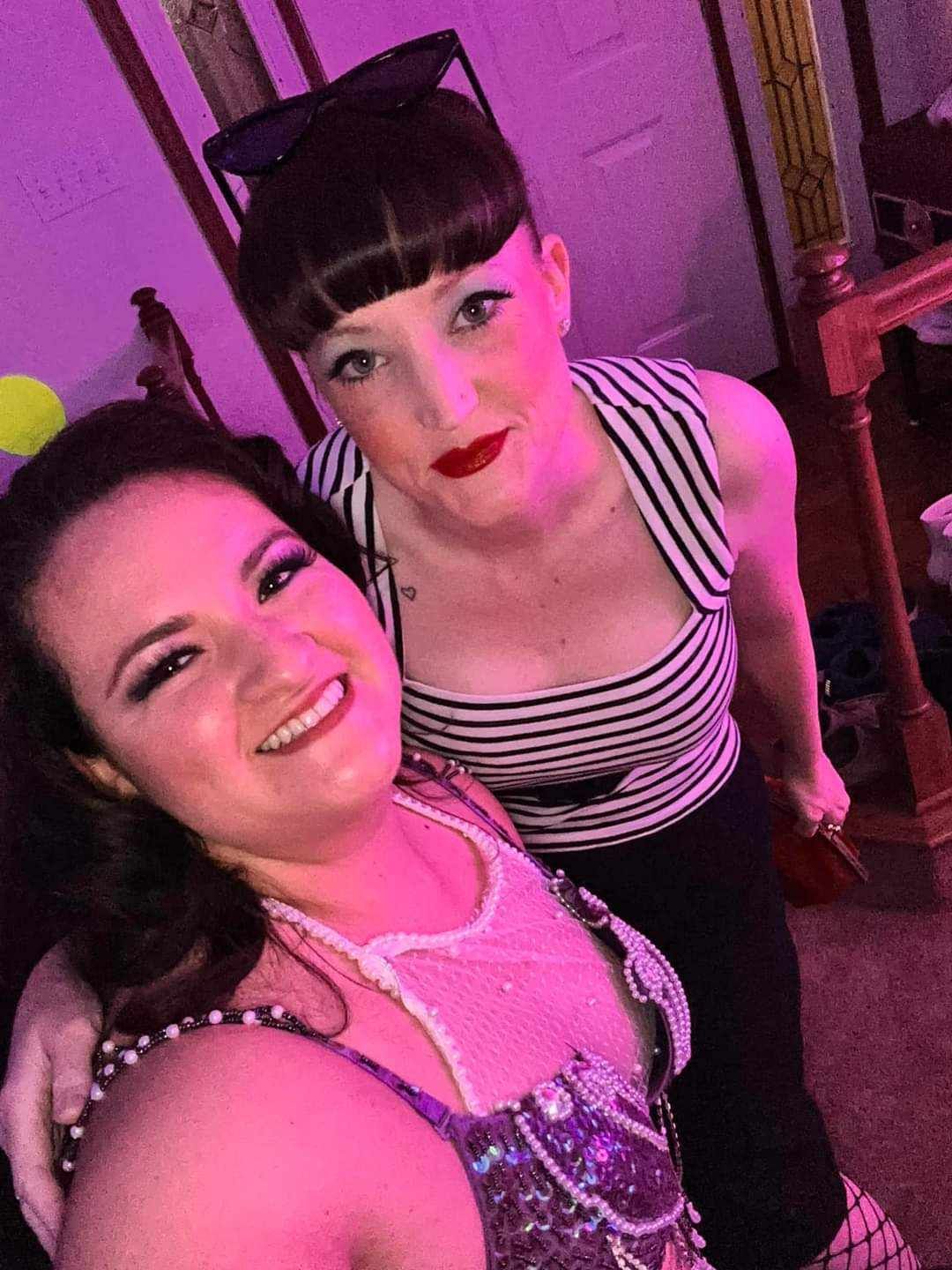 Two women are posing for a picture together in a room with purple lights.