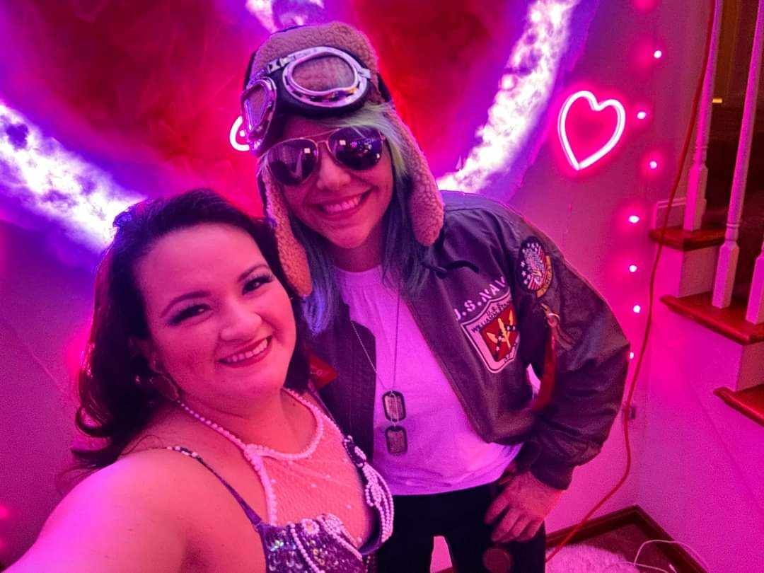 Two women are posing for a picture in front of a neon sign.