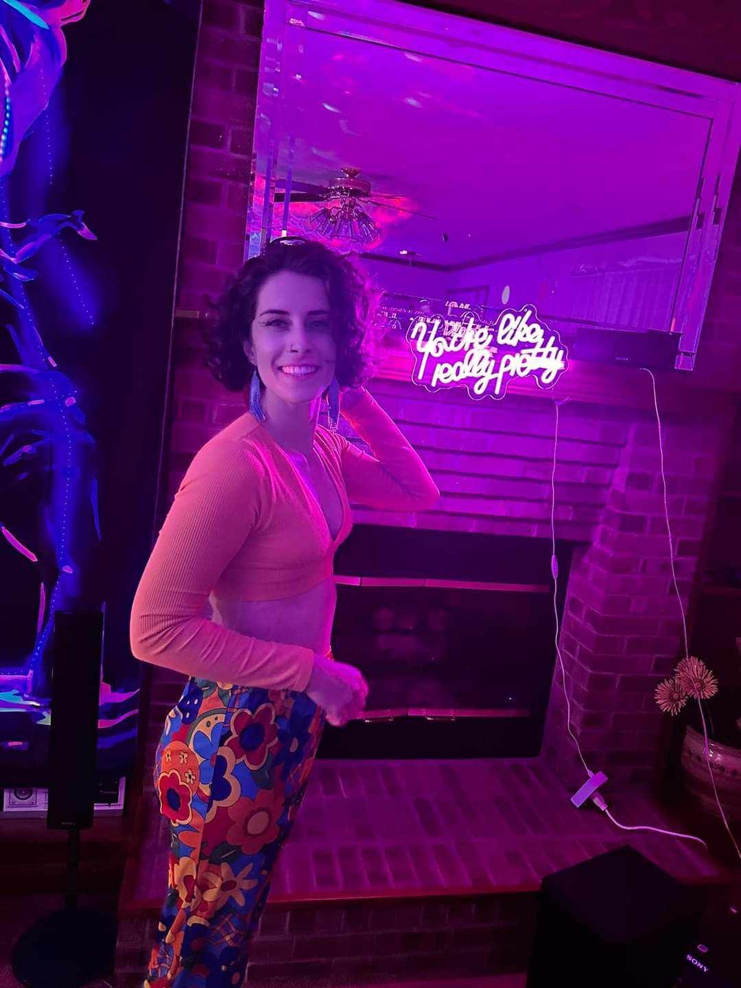 A woman is standing in front of a neon sign in a room.