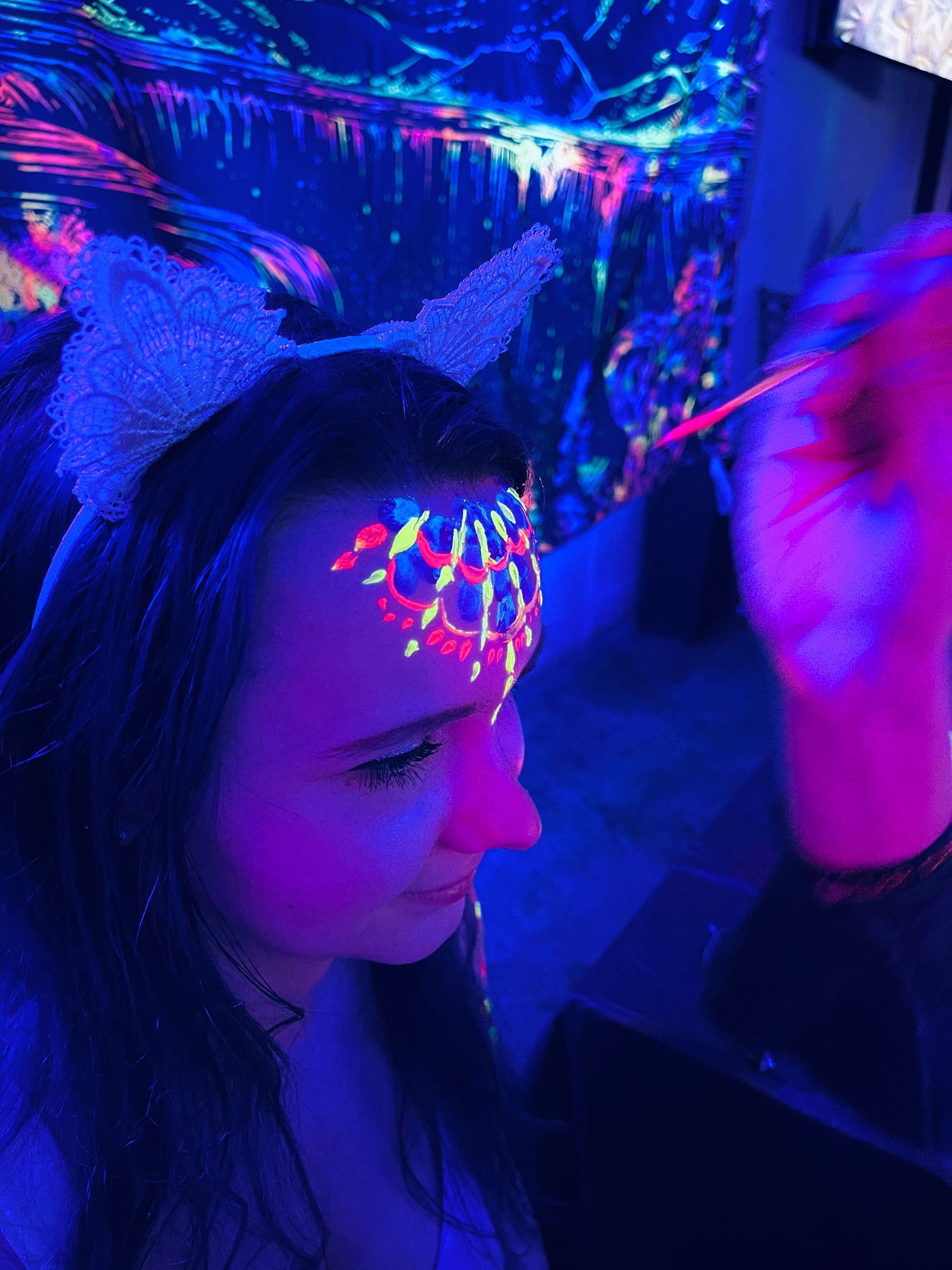 A woman is getting her face painted with glow in the dark paint.