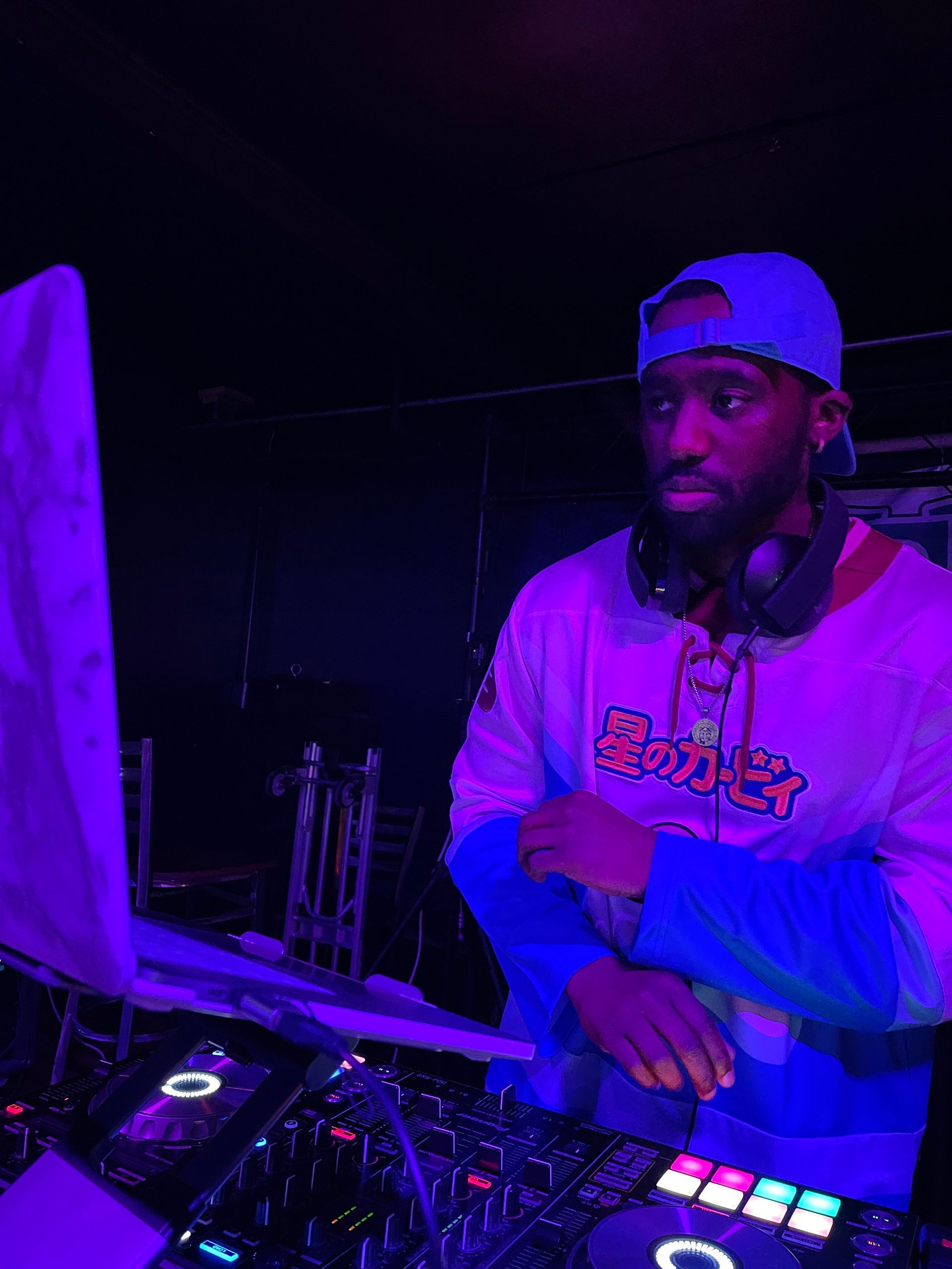 A man wearing headphones is standing in front of a computer in a dark room.