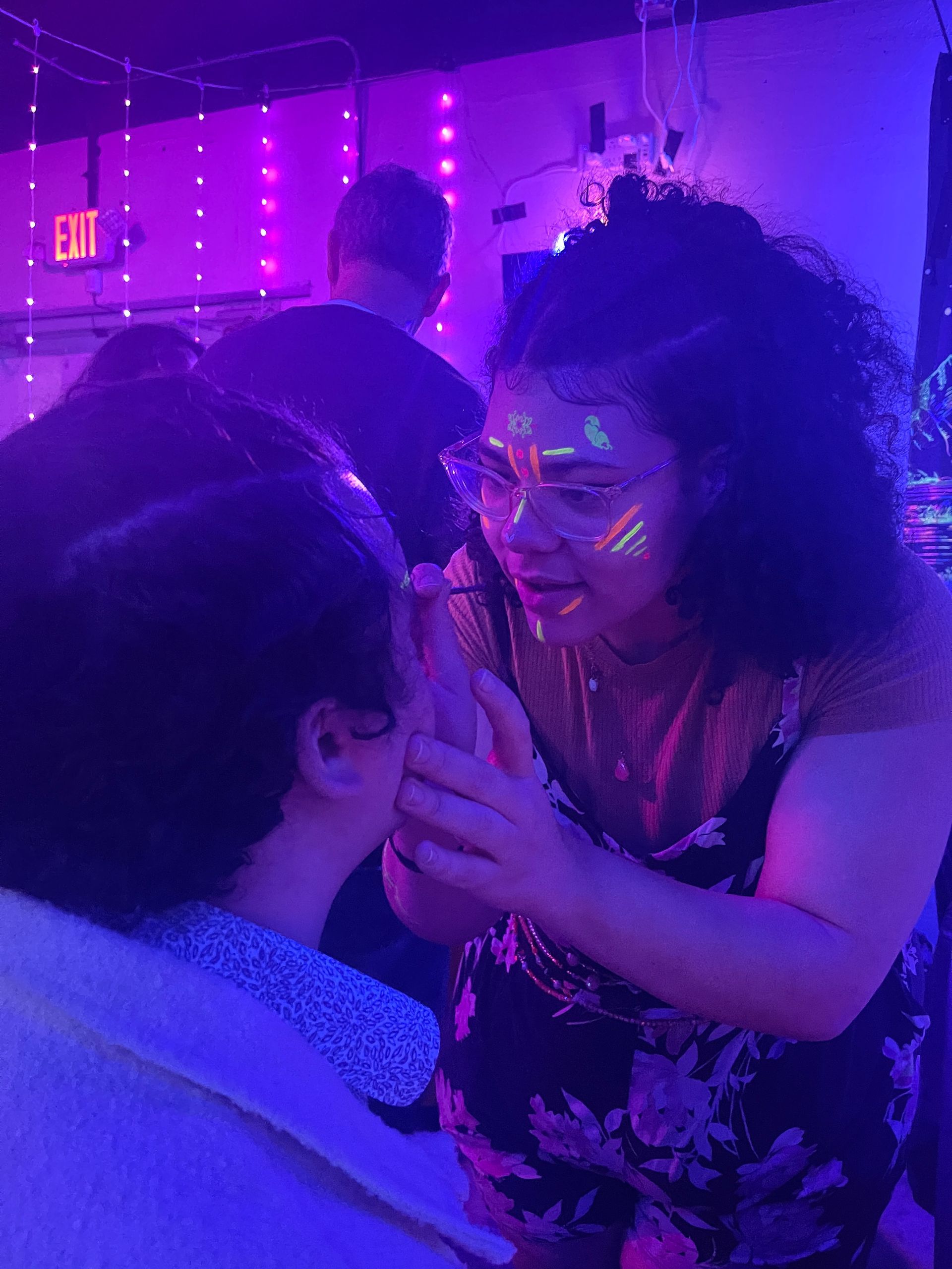 A woman is applying glow in the dark paint to a man 's face.