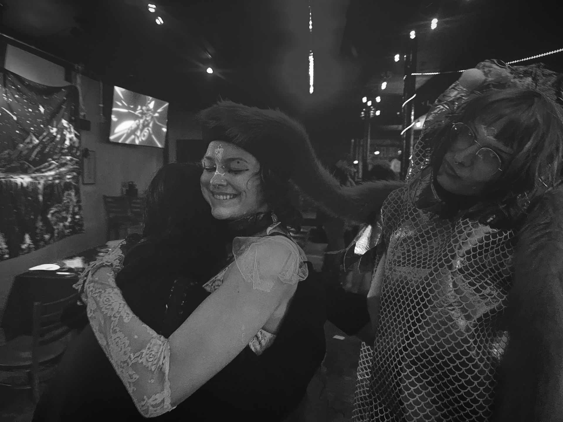 A black and white photo of two friends hugging each other in a dark room.