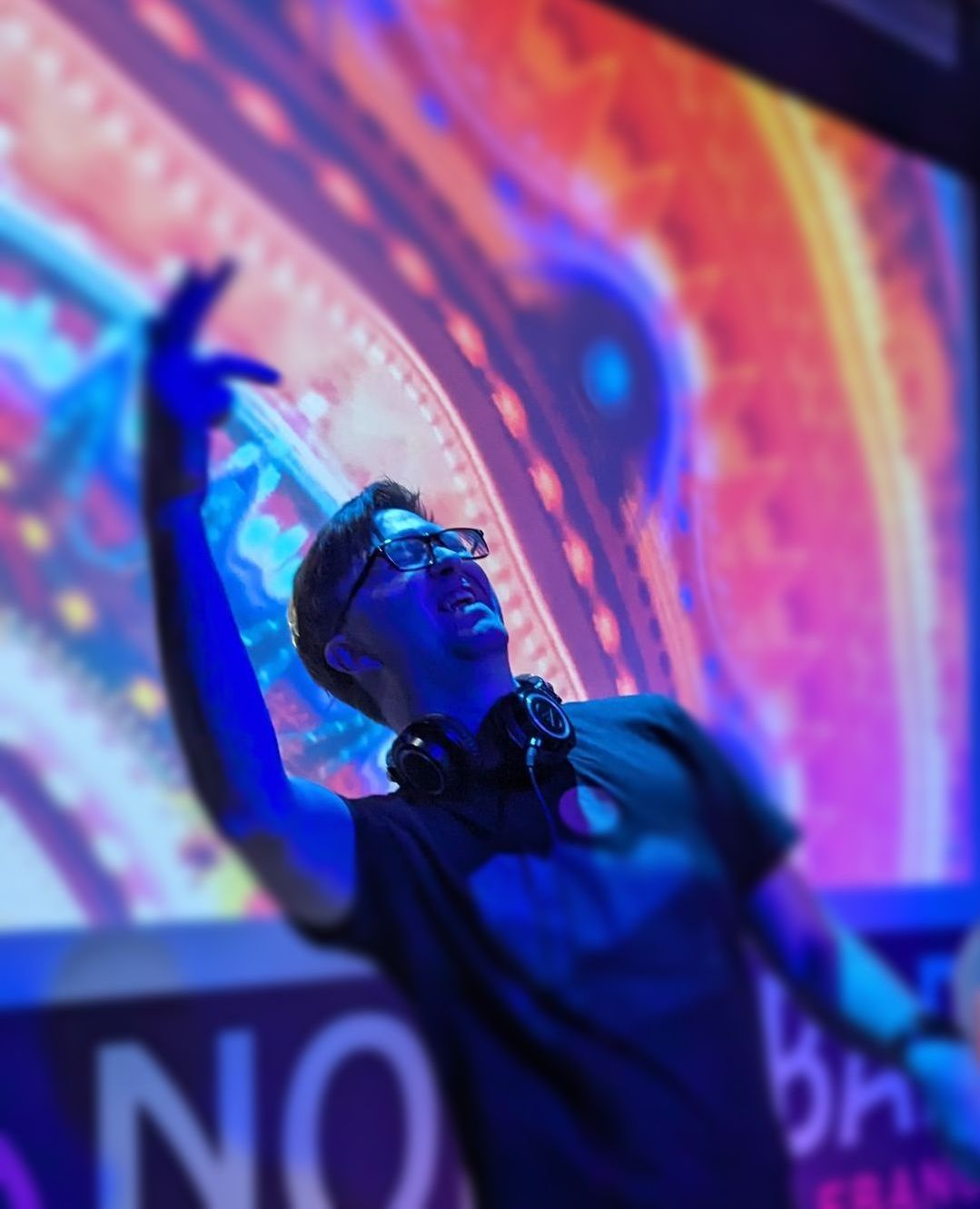 Dante is wearing headphones stands in front of a large screen.