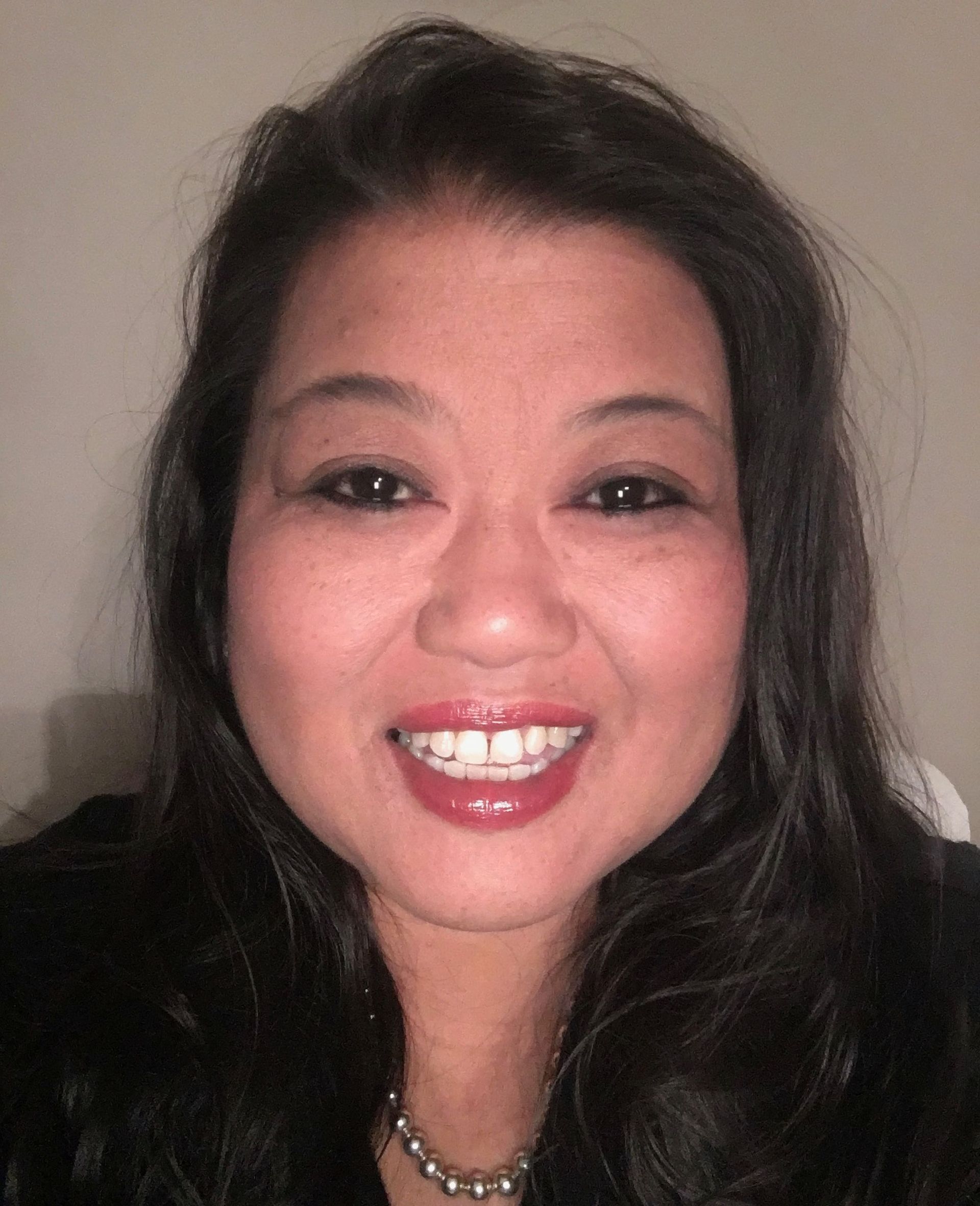 A woman with long hair is smiling and wearing a necklace