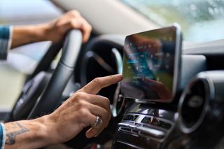 A man is driving a car and pressing a button on the dashboard.