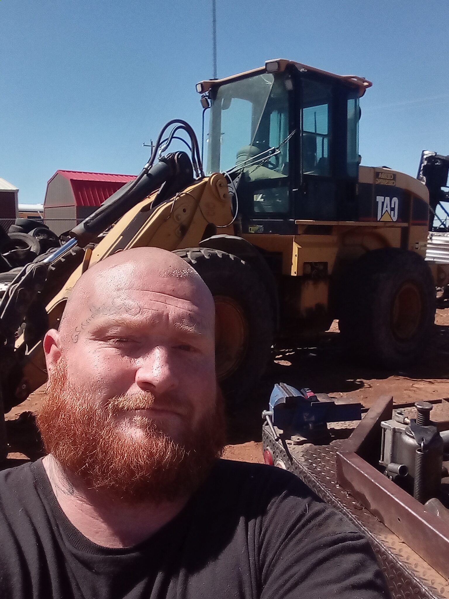 A man with a beard is taking a selfie in front of a cat tractor