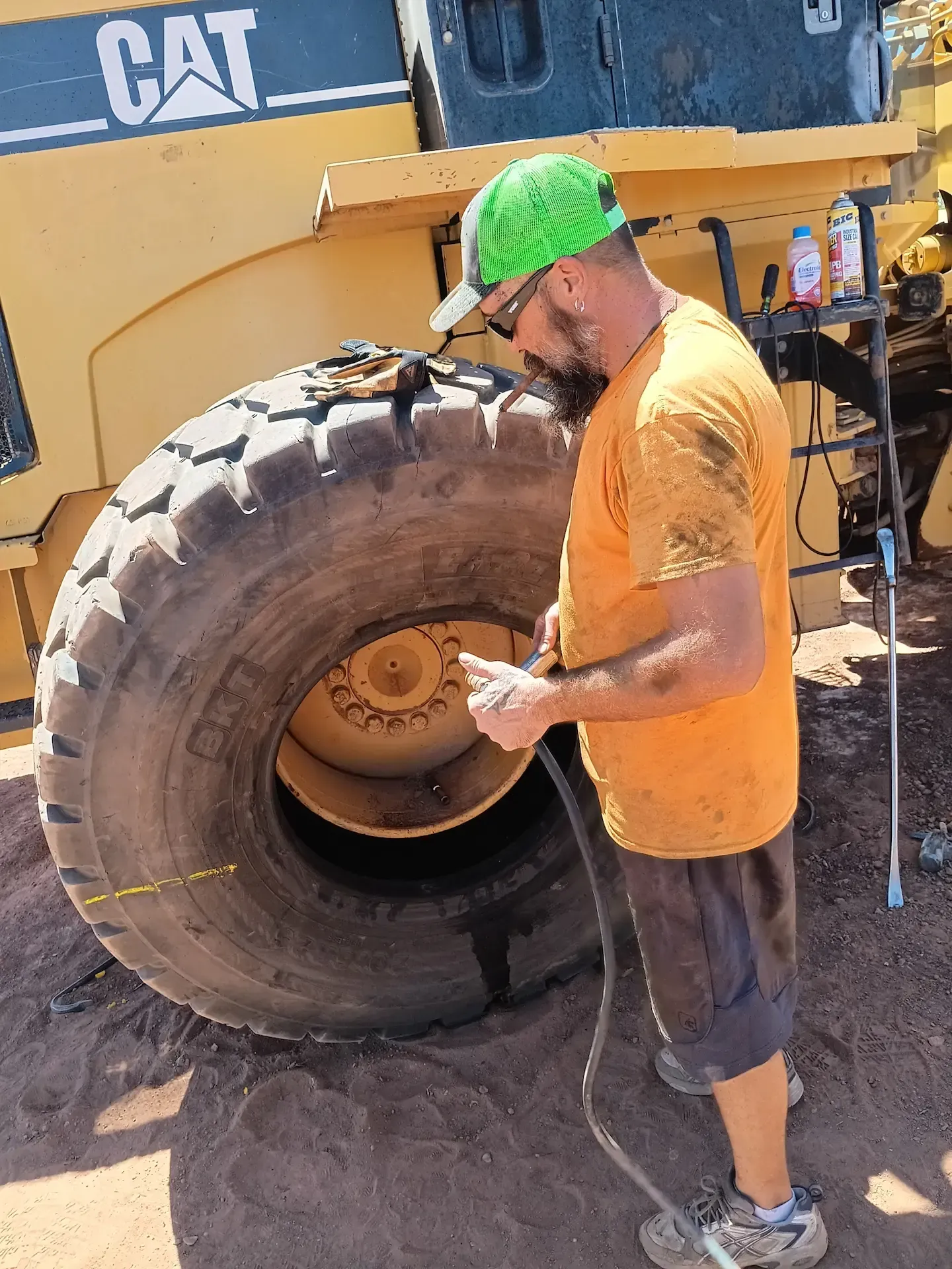 A man is standing next to a large cat tire.
